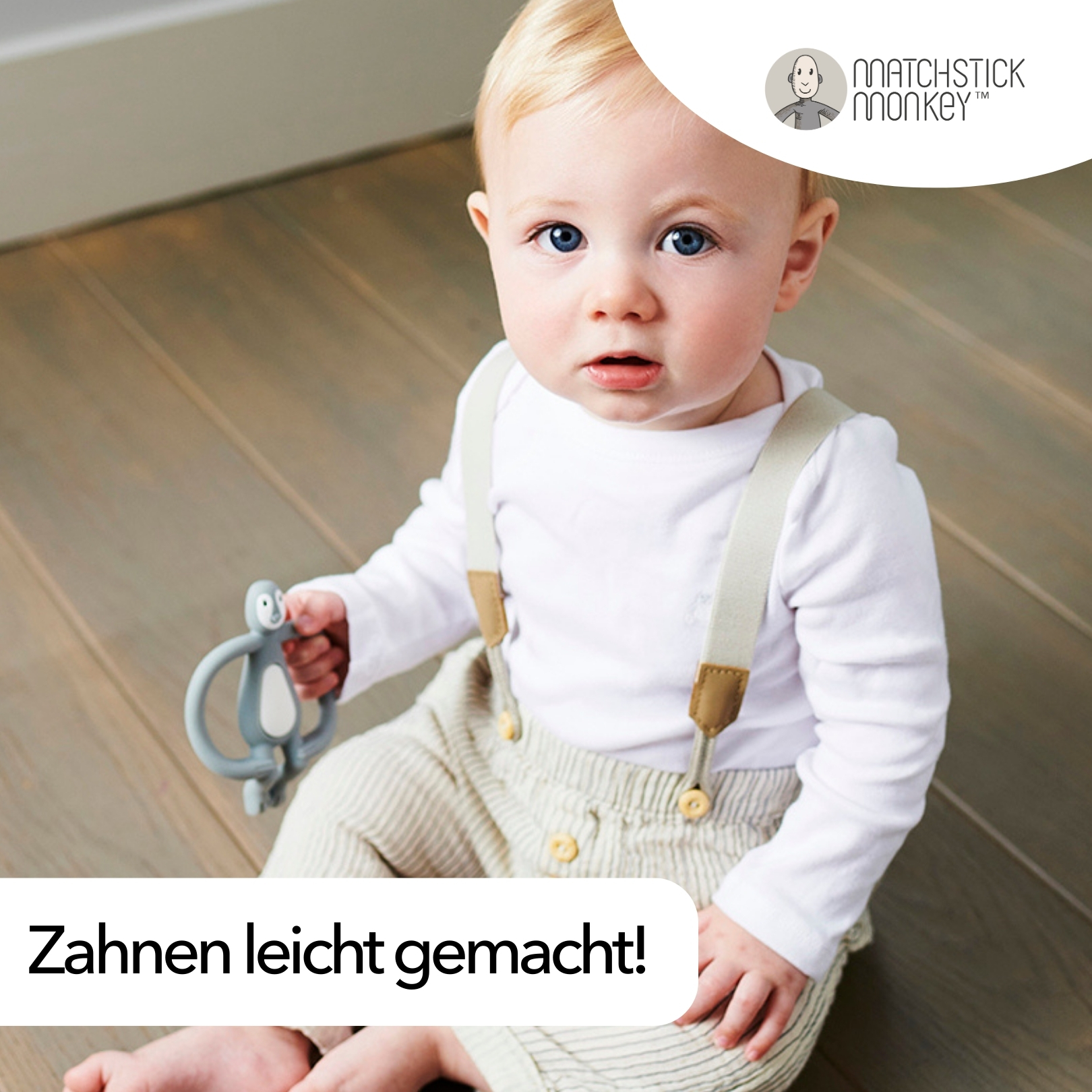 Ein Baby mit blauen Augen, das ein weißes Hemd und Hosenträger trägt, hält einen grauen, affenförmigen Beißring.