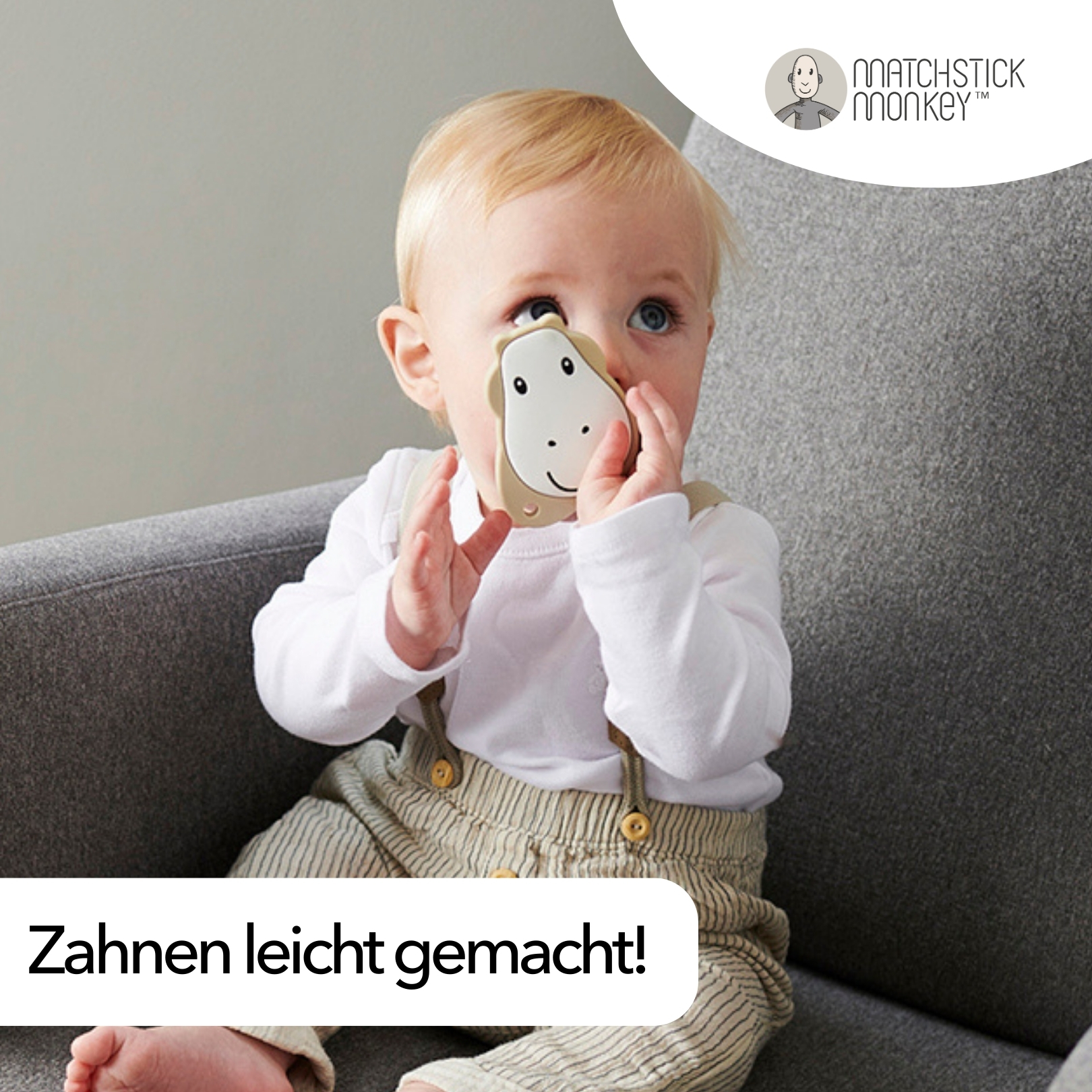 Baby hält ein beiges Beißspielzeug und sitzt auf einem grauen Sofa.