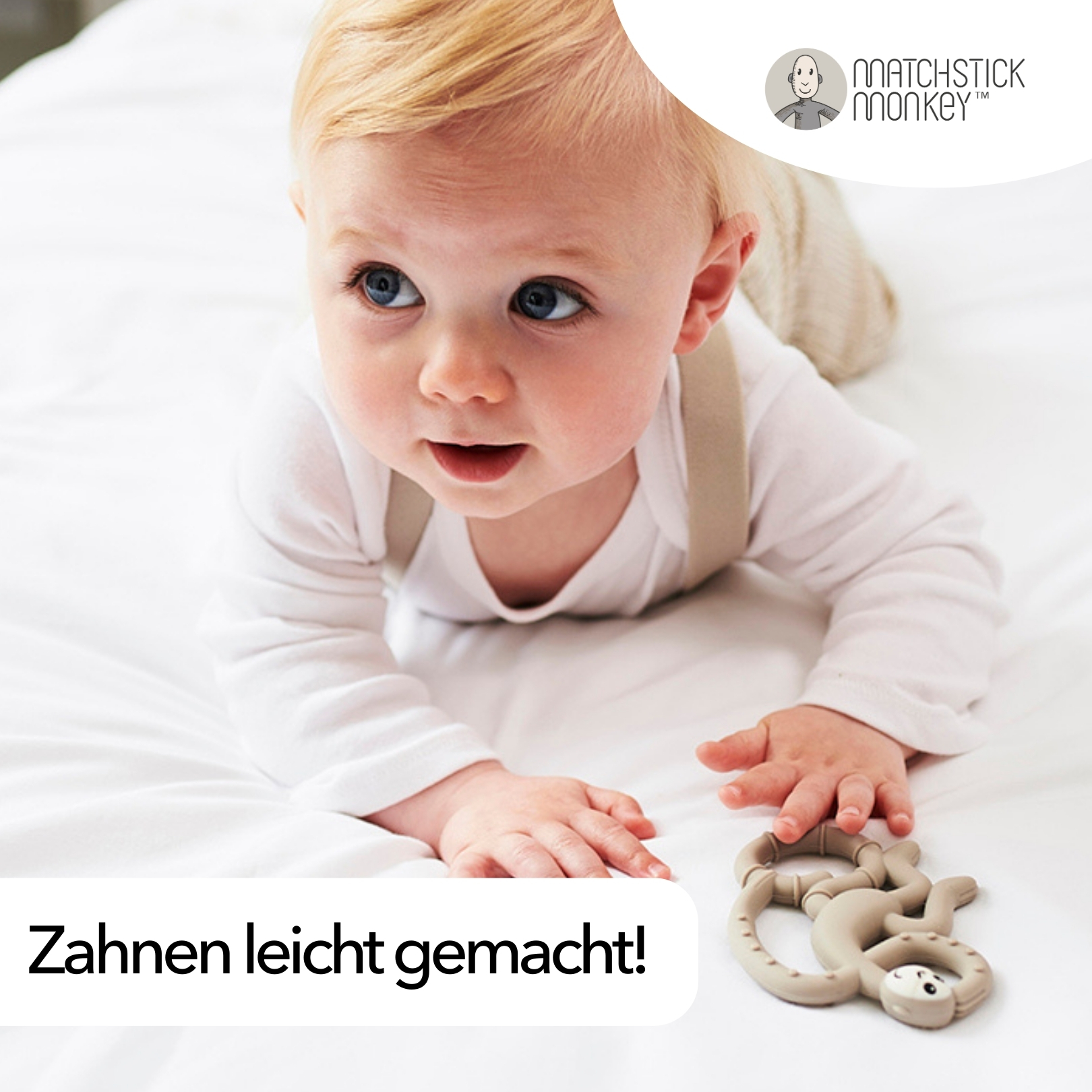 Baby liegt mit einem Affen-Beißring auf einem weißen Bett.
