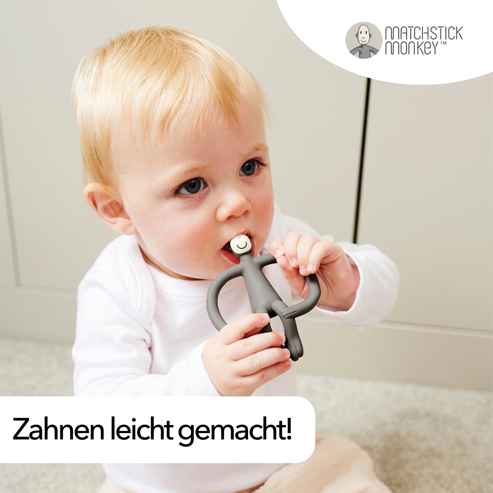 Ein Baby mit einem Beißring im Mund. Das Spielzeug ist grau und affenförmig.