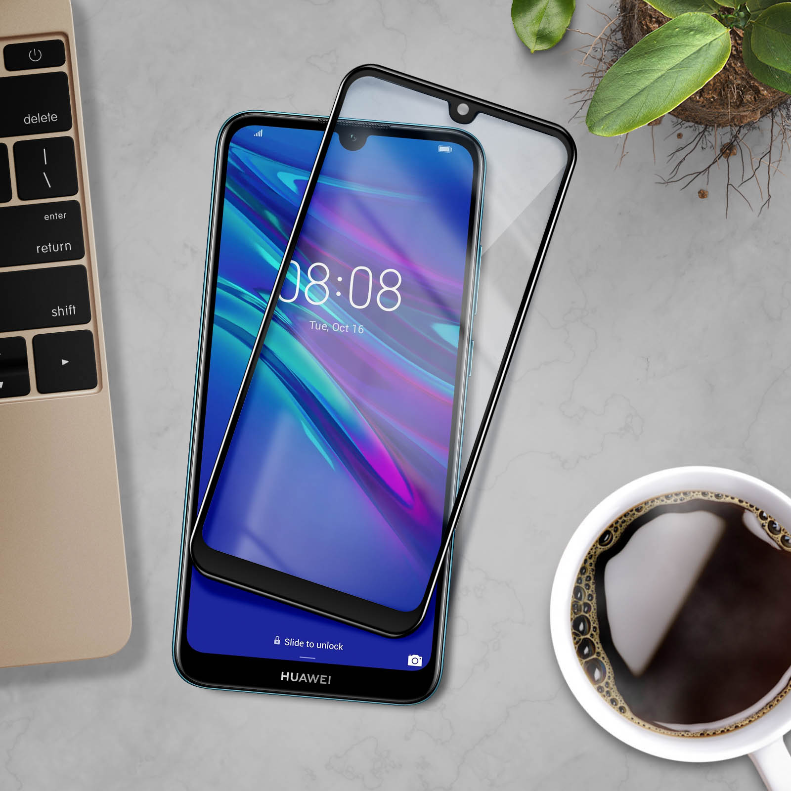 Smartphone con protezione schermo e tazza di caffè su un tavolo con tastiera e pianta.