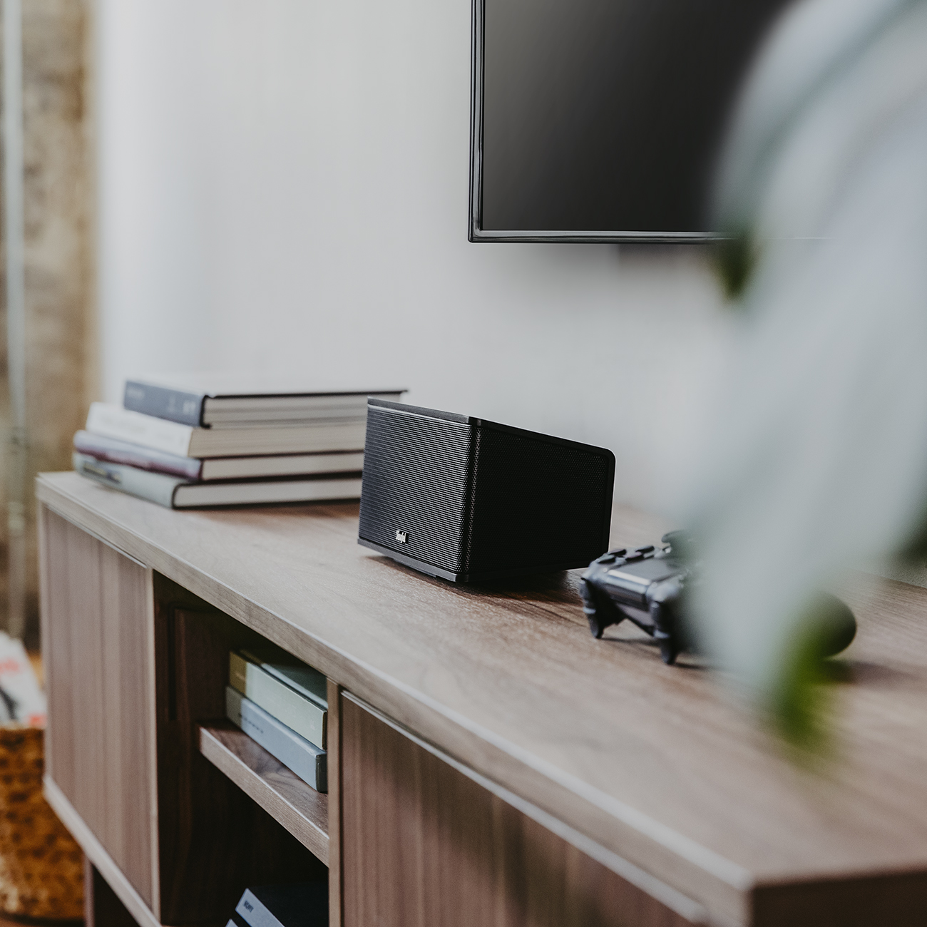 Schwarzer Lautsprecher auf einem Holzschrank. Ein Fernseher ist oben. Bücher und eine Spielkonsole sind ebenfalls auf dem Schrank.