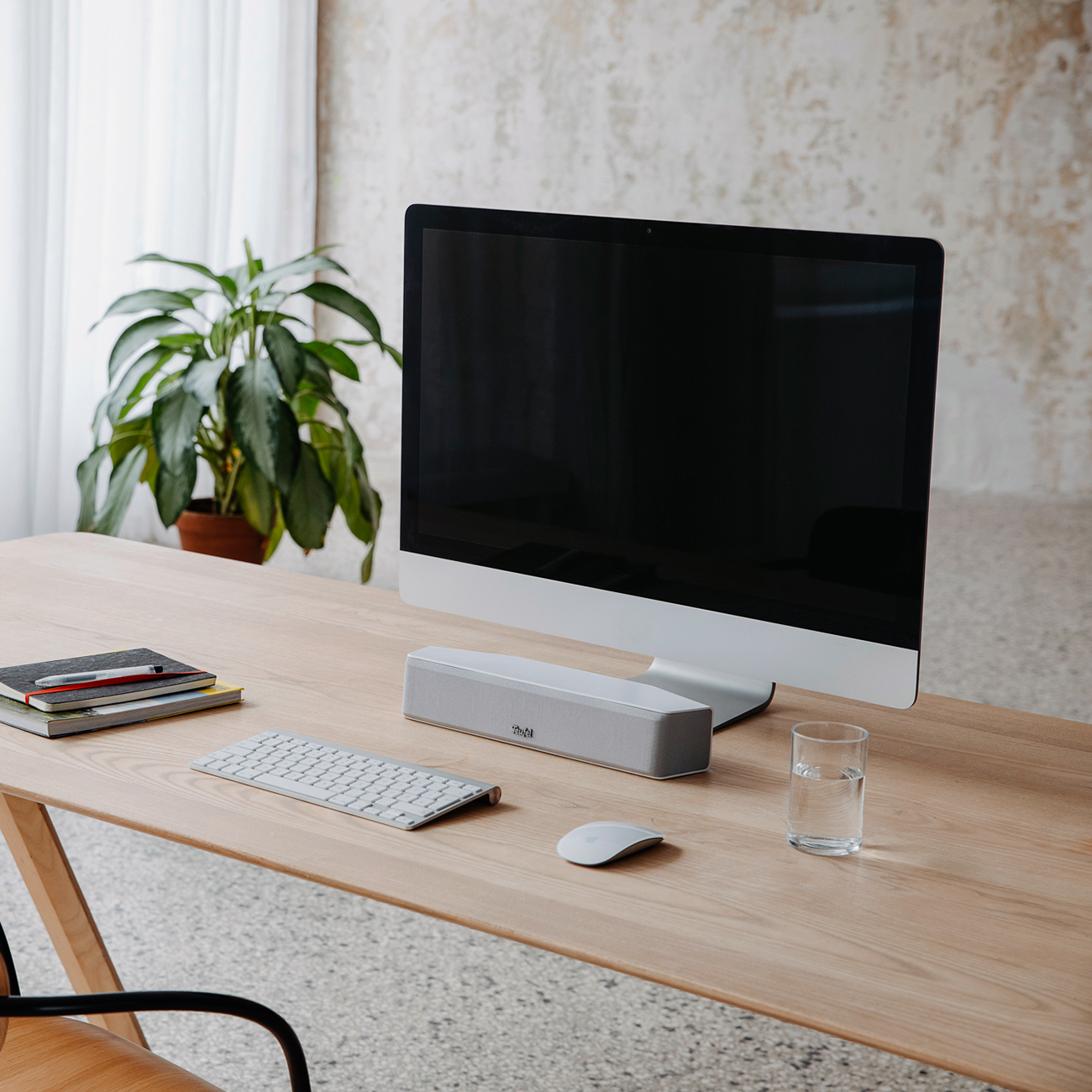 Een bureau met een computer, toetsenbord, muis, luidspreker en een glas water. Een plant staat op de achtergrond.
