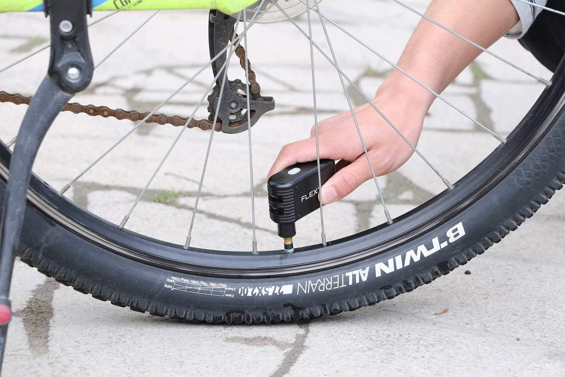 Eine Person pumpt einen Fahrradreifen auf, Nahaufnahme. Der Reifen ist schwarz mit weißem Text, auf Beton.