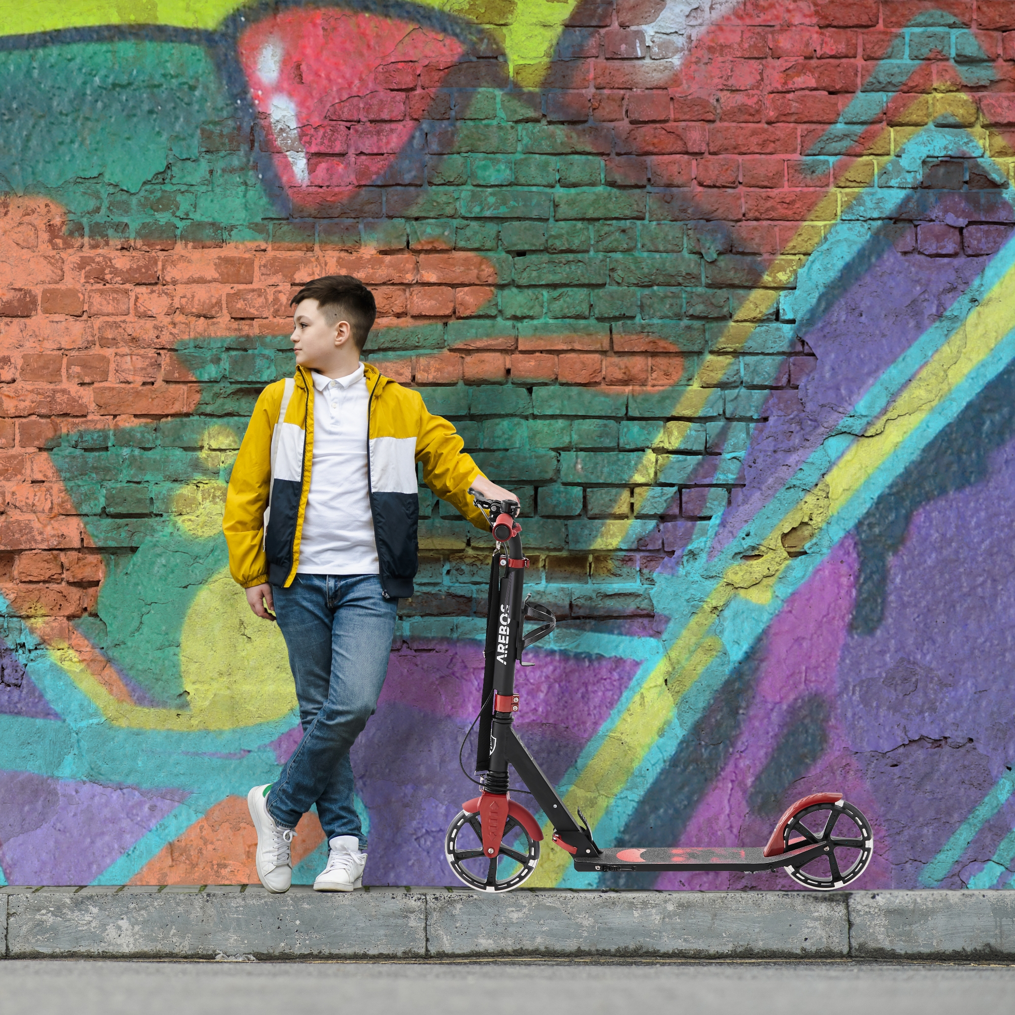 Junge mit gelber Jacke und Jeans steht neben einem Roller an Graffiti-Wand.