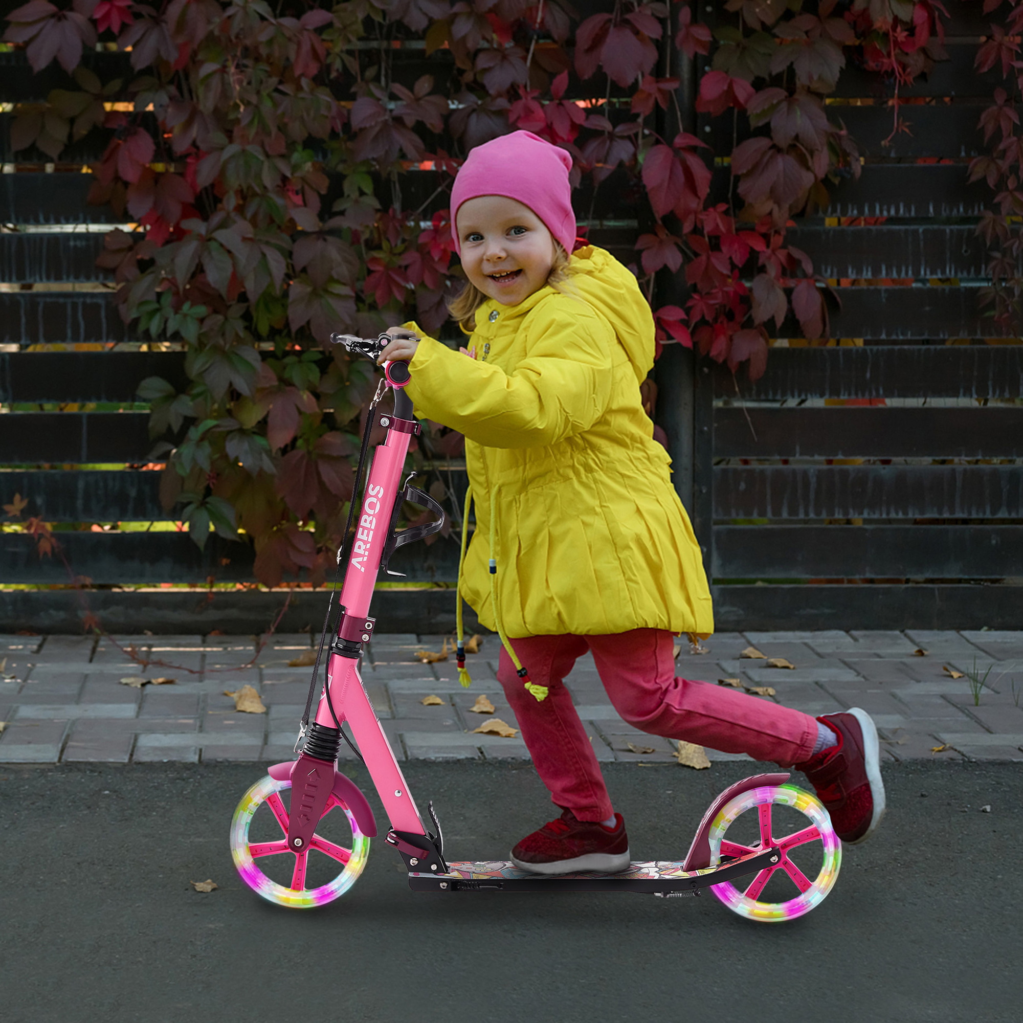 Junges Mädchen in gelber Jacke und rosa Mütze fährt rosa Roller mit LED-Lichtern.