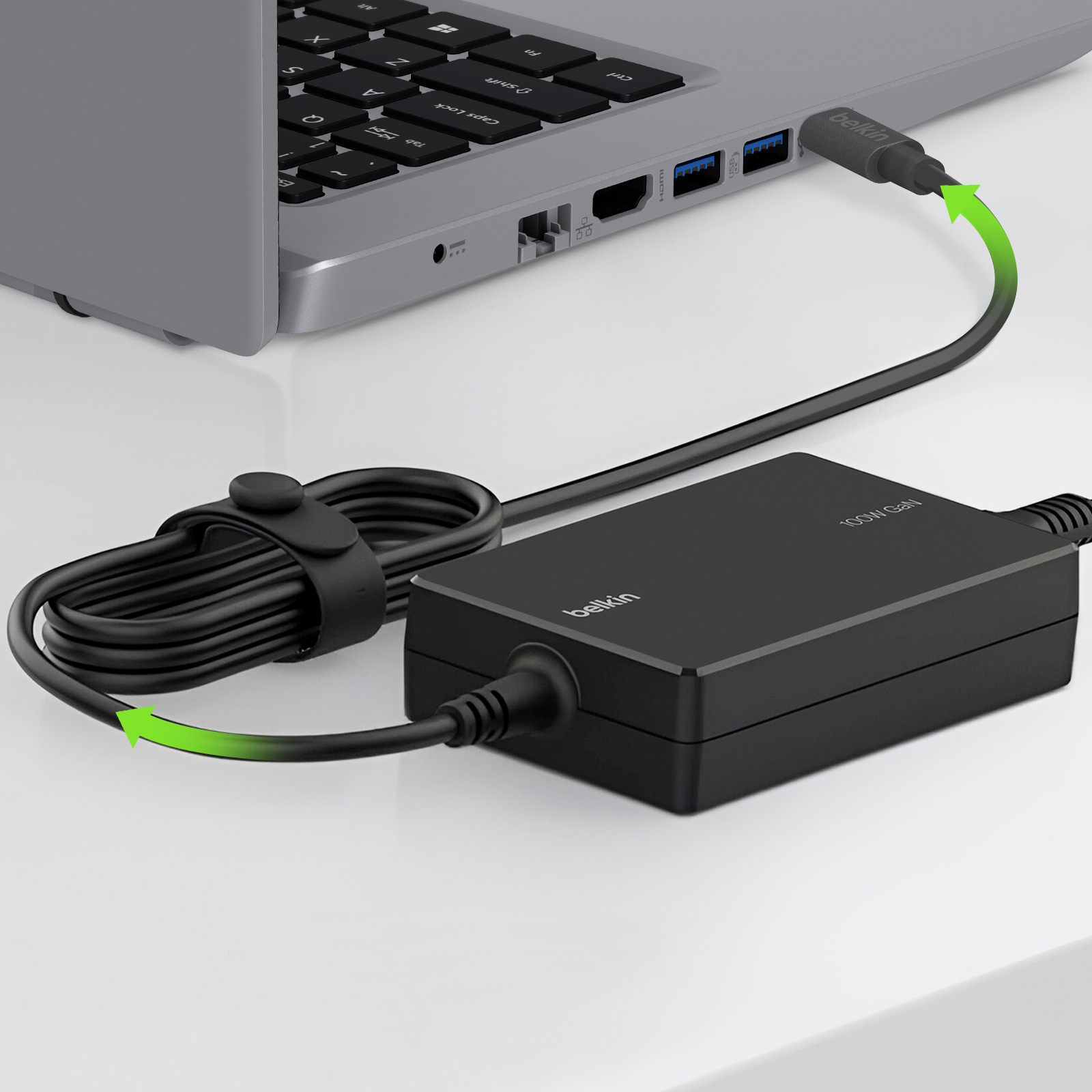 Caricatore e cavo Belkin neri collegati a un laptop. Frecce verdi mostrano la connessione.