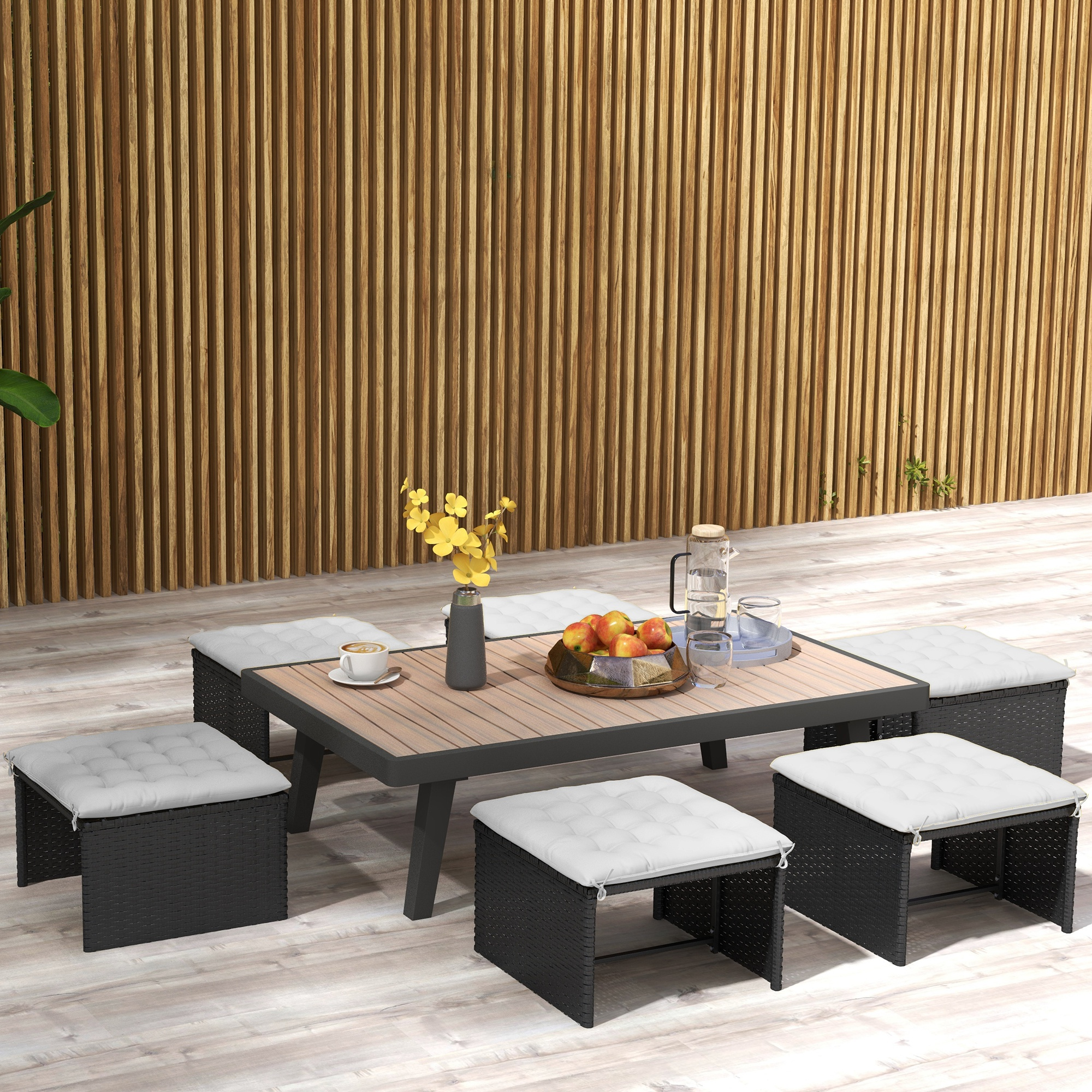 Outdoor-Sitzarrangement mit vier schwarzen Korbstühlen, Tisch und Dekoration mit Holzuntergrund.