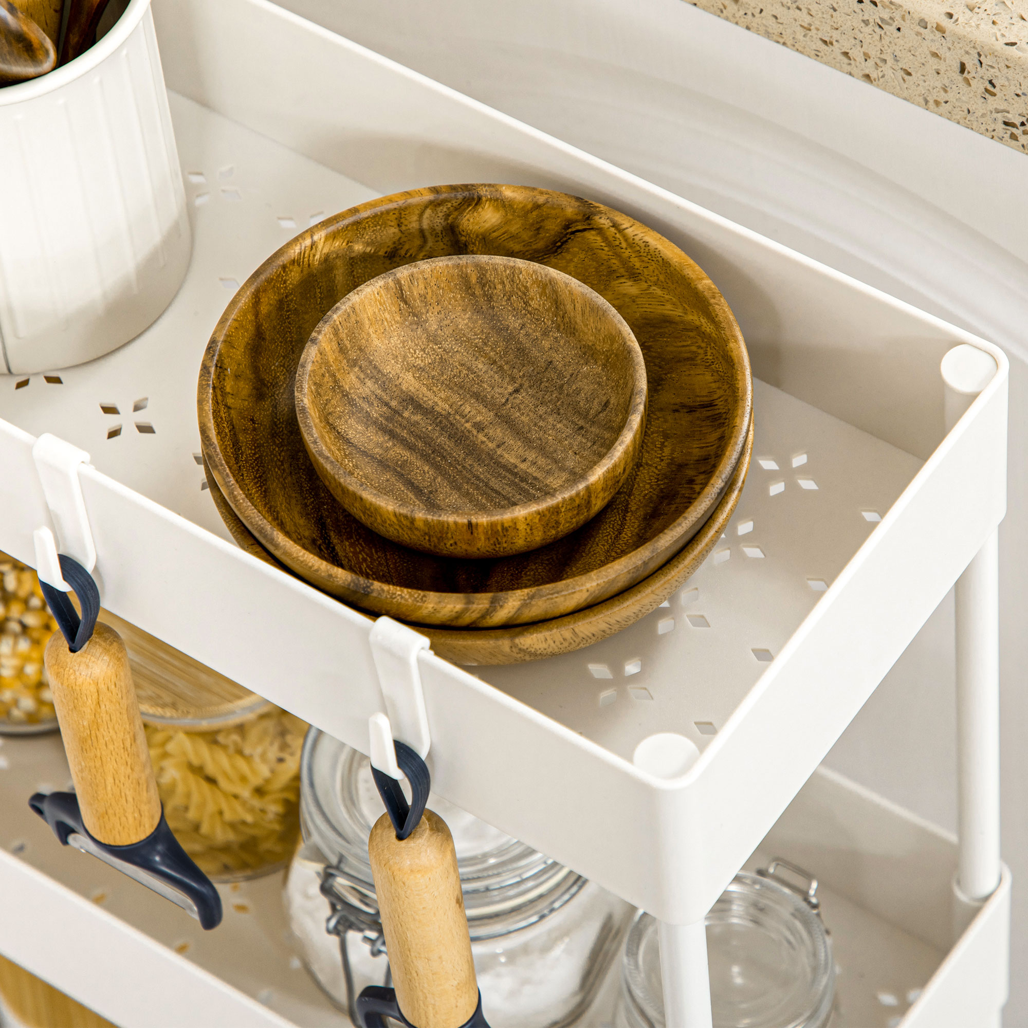 Un carrito de cocina blanco con cuencos de madera y utensilios. Se ven tarros de comida y otros objetos.