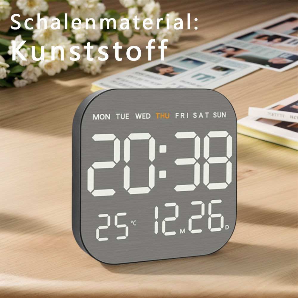 Digitaluhr zeigt Zeit, Datum und Tag. Auf einem Holztisch mit Blumen und Gegenständen im Hintergrund.
