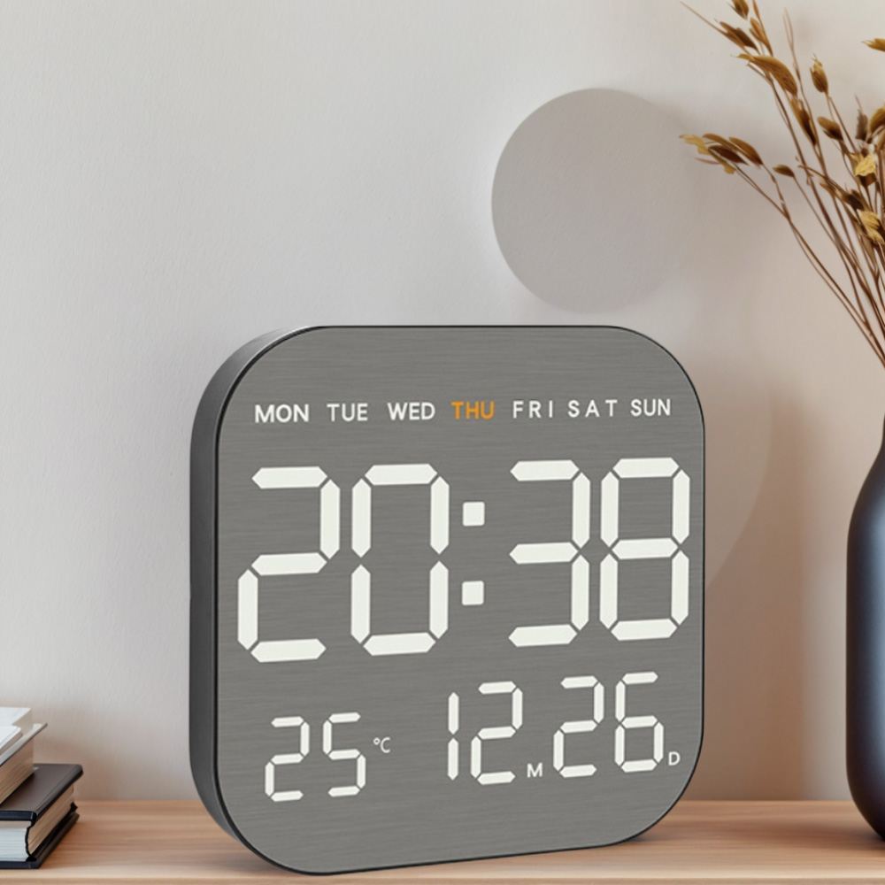 Eine graue Digitaluhr zeigt 20:38, 25°C und 12.26 an. Sie steht auf Holz.