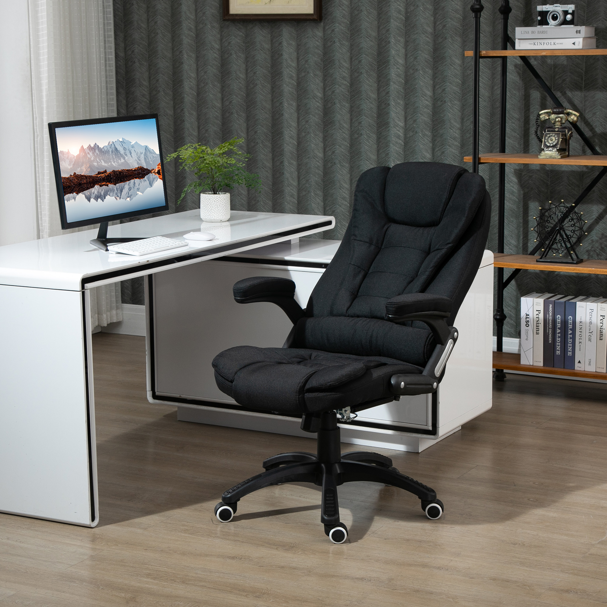 Schwarzer Bürostuhl in einem Home-Office. Ein Computer, ein Schreibtisch und eine Pflanze sind im Hintergrund.
