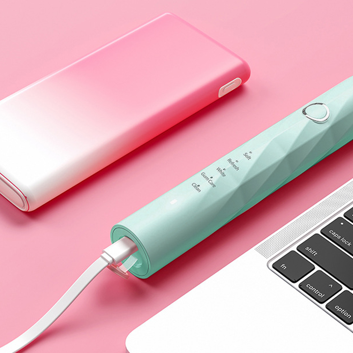 Elektrische Zahnbürste wird geladen, neben einer rosa Powerbank und einem Laptop. Weißes Ladekabel.
