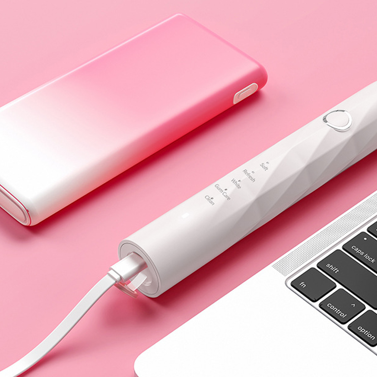 Weißes und rosa Zahnbürstenladegerät mit einer Zahnbürste neben einem Laptop auf rosa Oberfläche.