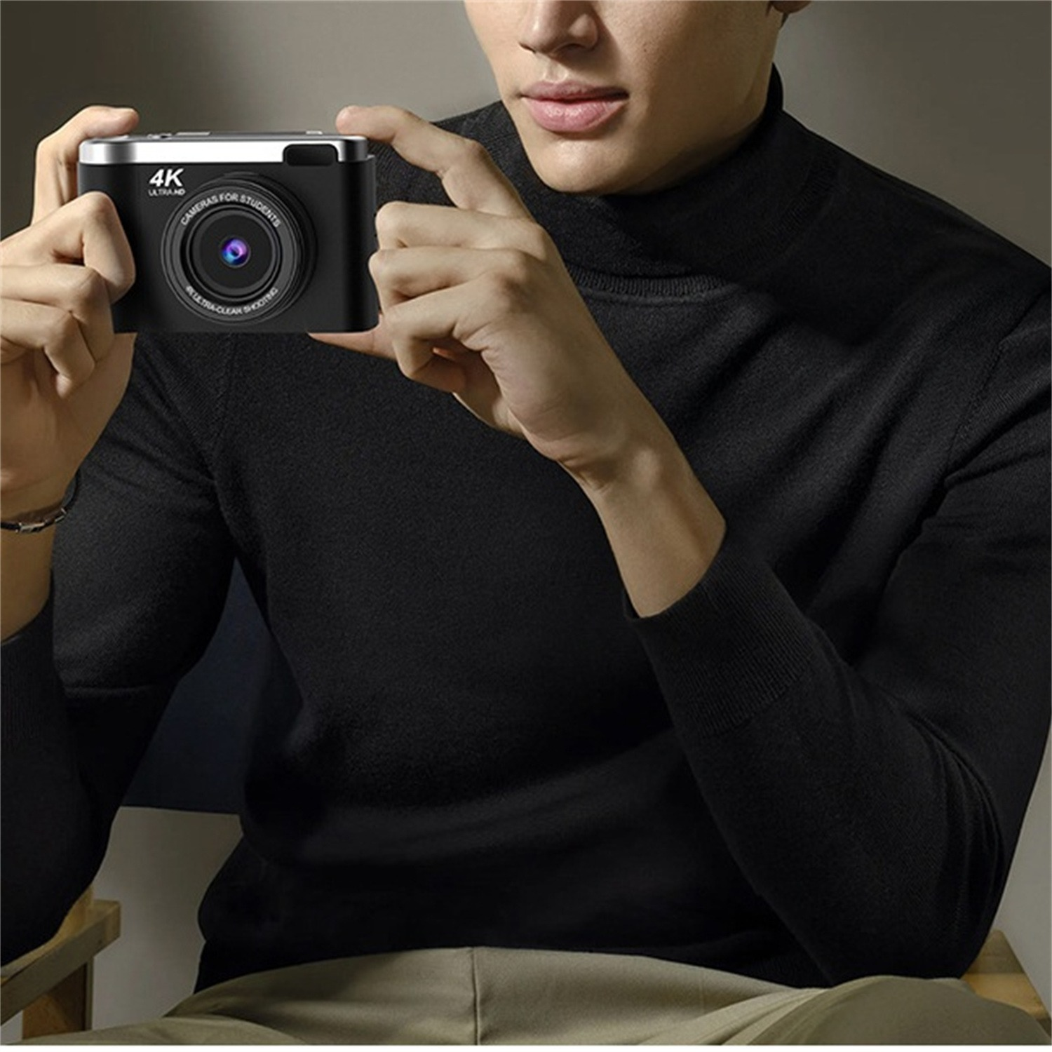 Mann hält eine schwarze Kamera. 4K Ultra HD, silbernes Oberteil, schwarzer Pullover.