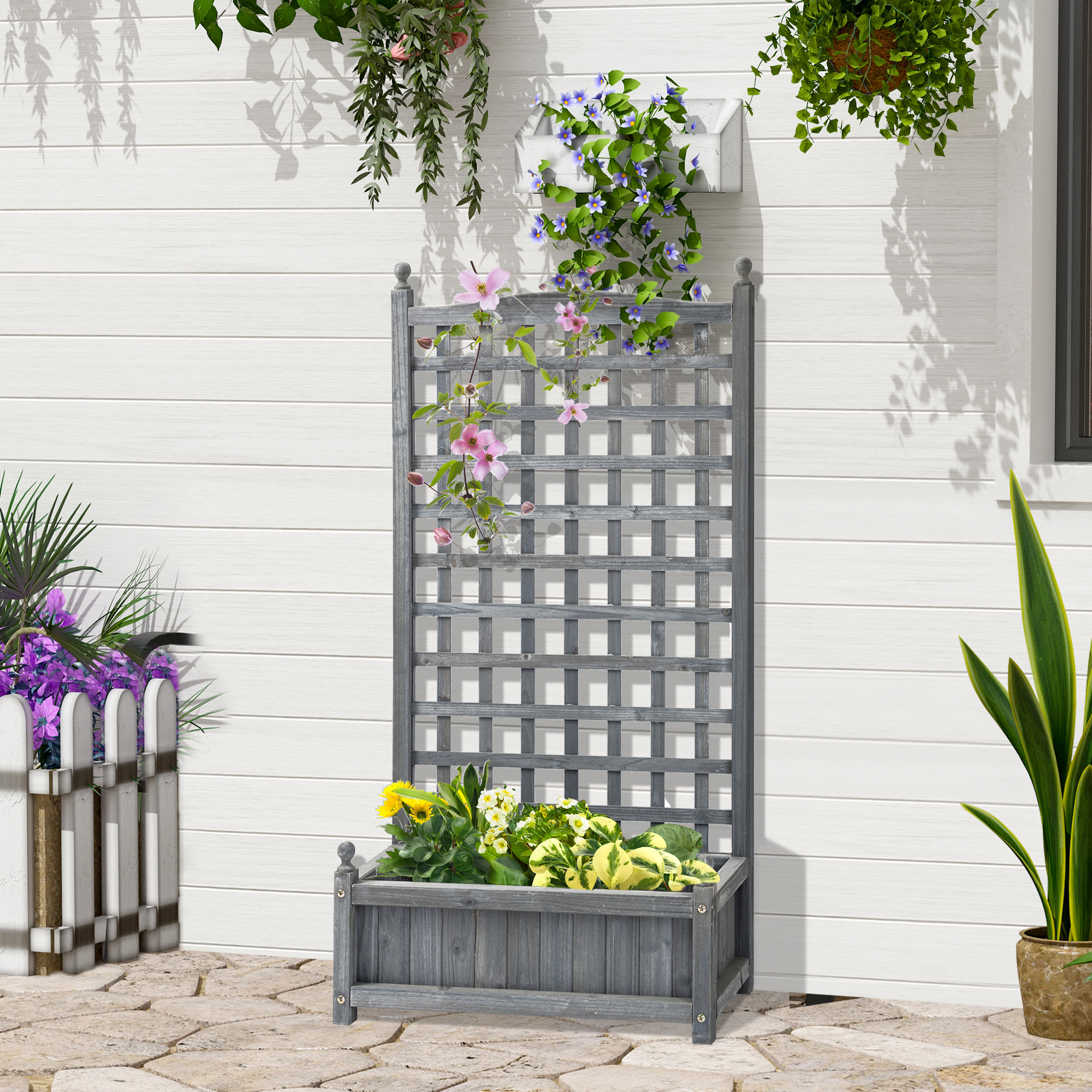 Ein graues Holzgitter mit einer Pflanzkasten und Blumen. Es steht vor einer weißen Wand.
