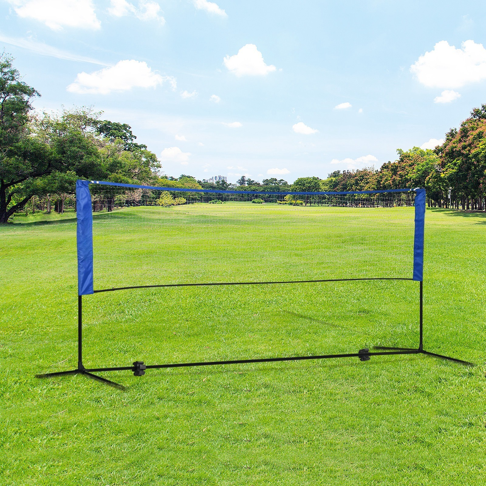 Badmintonnetz auf grünem Gras, unter blauem Himmel mit Wolken und Bäumen im Hintergrund.