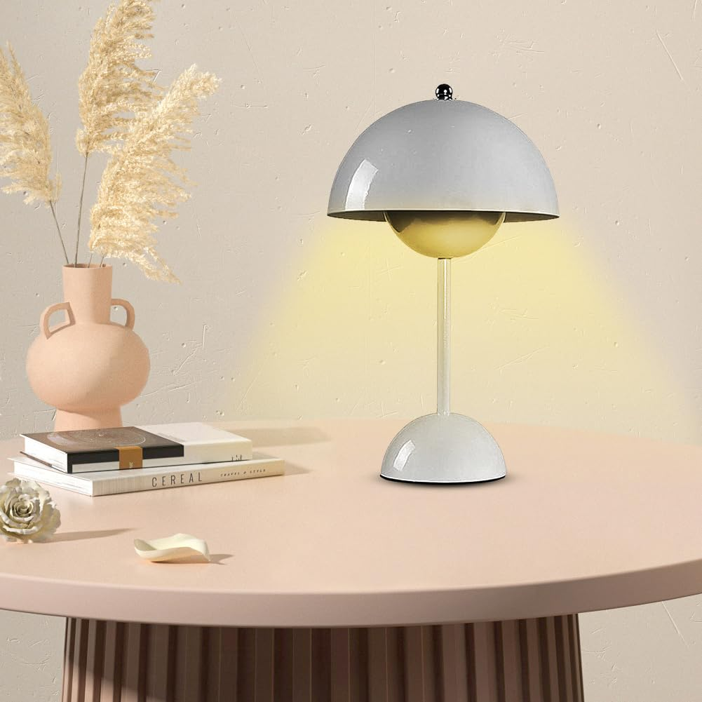 Weiße Tischlampe mit grauem Dom und Sockel auf einem rosa Tisch. Vase und Bücher sind ebenfalls vorhanden.