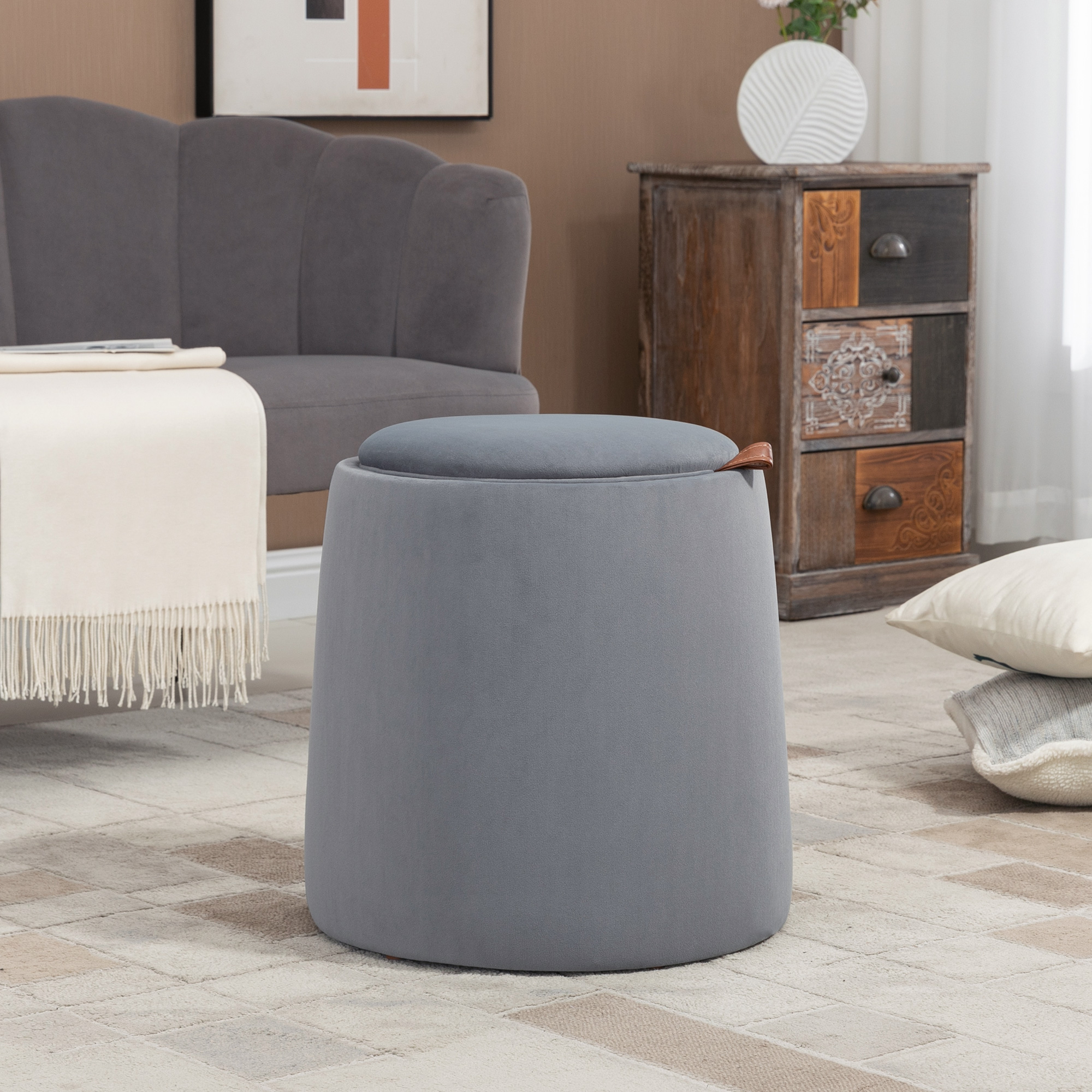 Grauer Hocker in einem Wohnzimmer. Eine Couch, ein Teppich und andere Möbel sind im Hintergrund sichtbar.