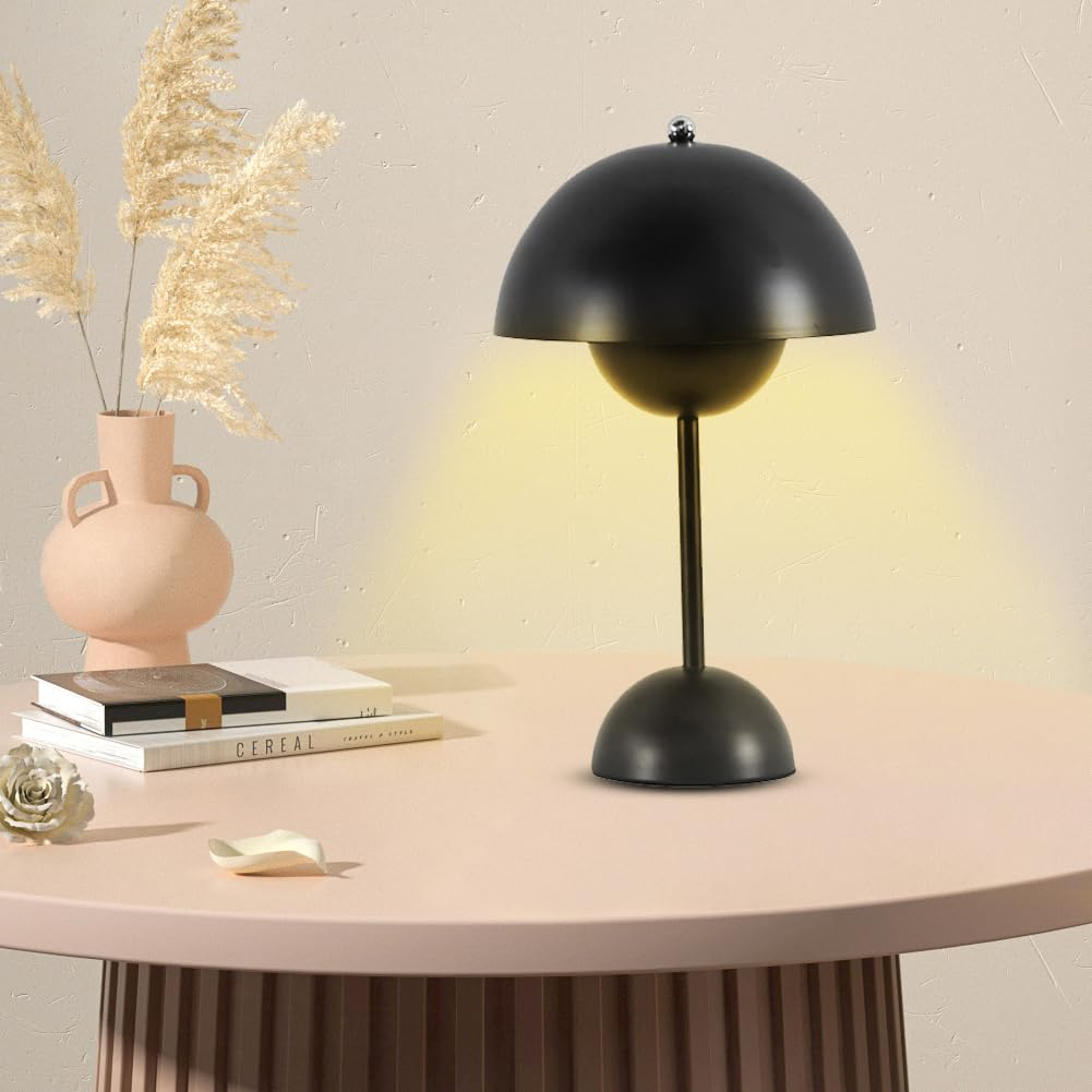 Schwarze Kuppellampe auf pinkem Tisch, neben Vasen und Büchern, gelbes Licht.