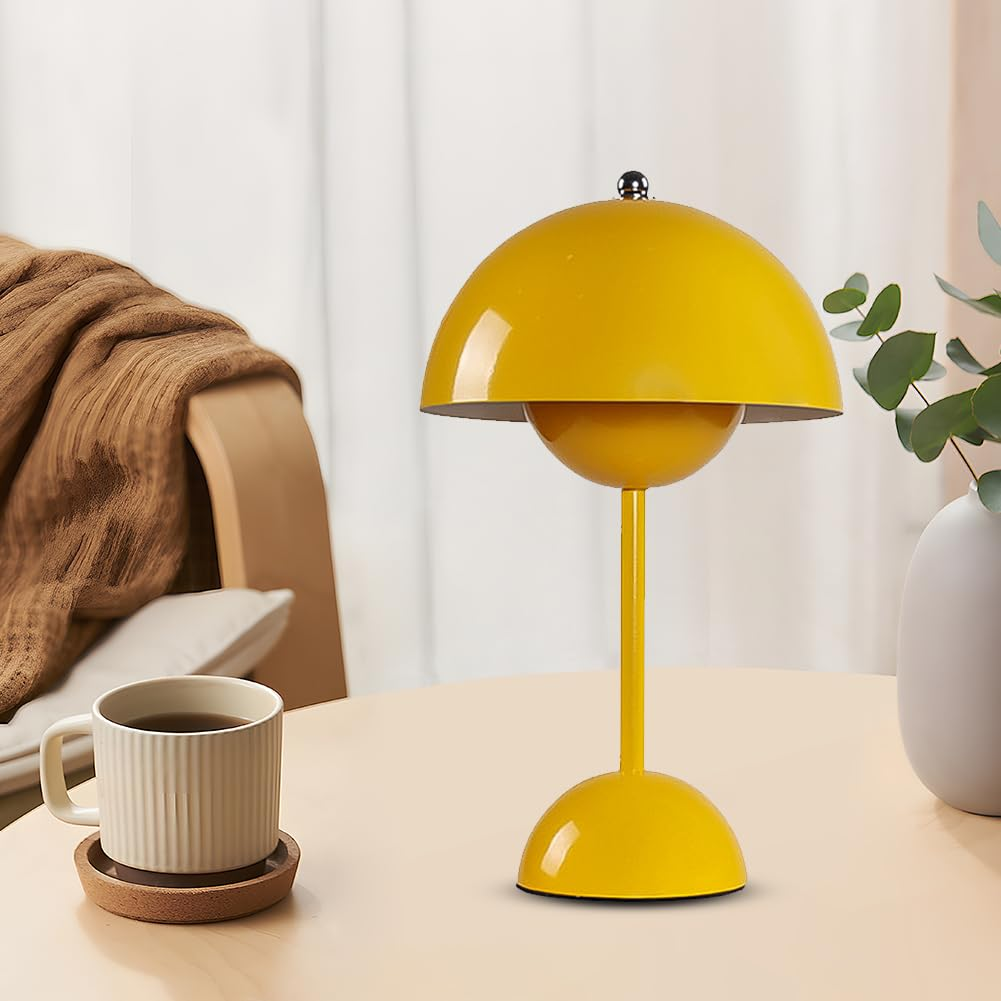 Eine gelbe Lampe, eine Tasse und ein Untersetzer auf einem runden Tisch, mit einer Vase und Pflanze im Hintergrund.