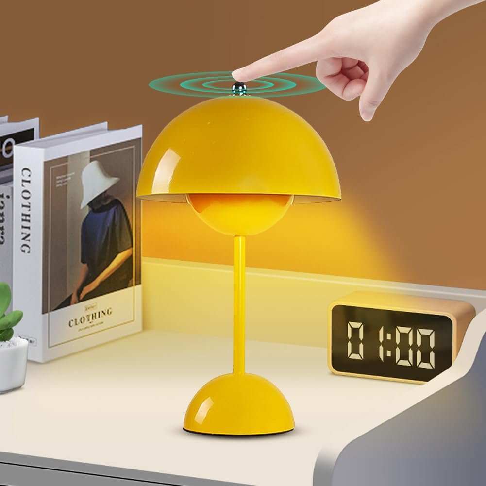 Gelbe Lampe auf einem Schreibtisch, eine Hand berührt die Oberseite. Eine Digitaluhr und Bücher sind im Hintergrund.