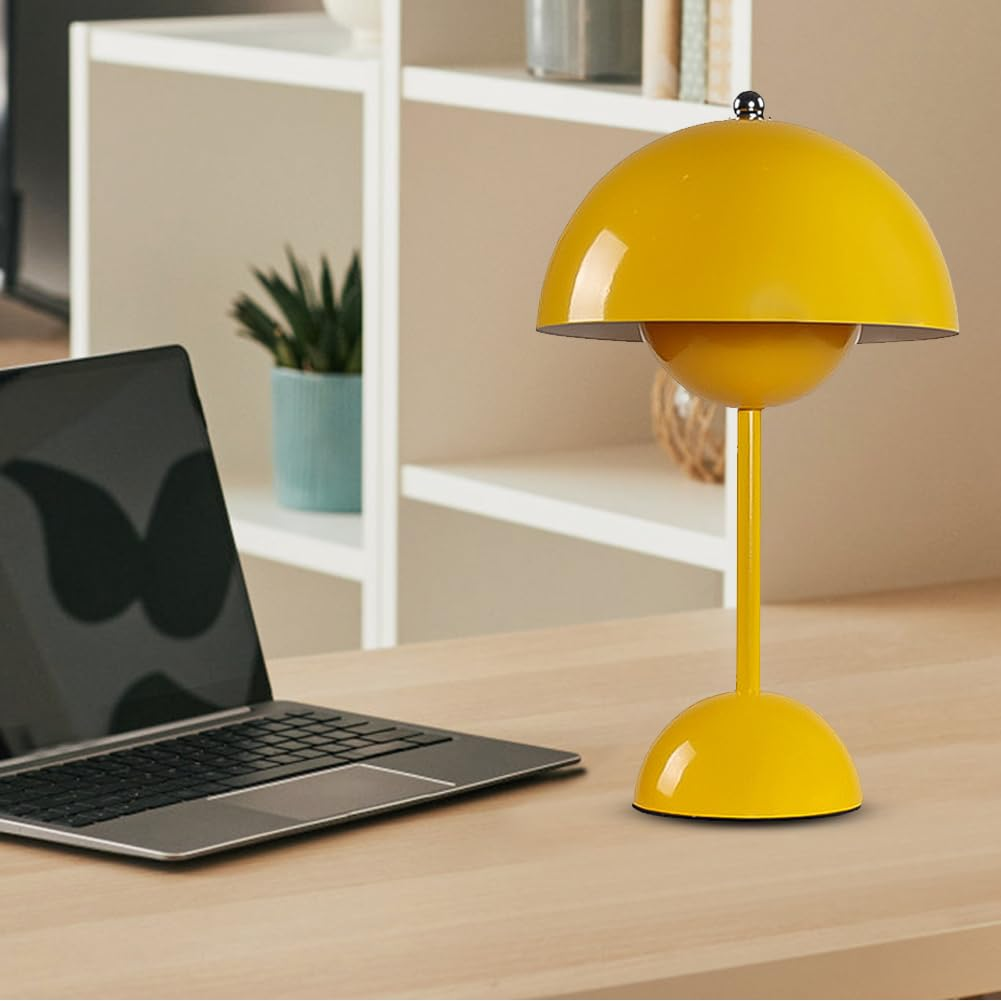 Eine gelbe Lampe auf einem Holzschreibtisch mit Laptop und Pflanze in blauem Topf. Bücher im Hintergrund.