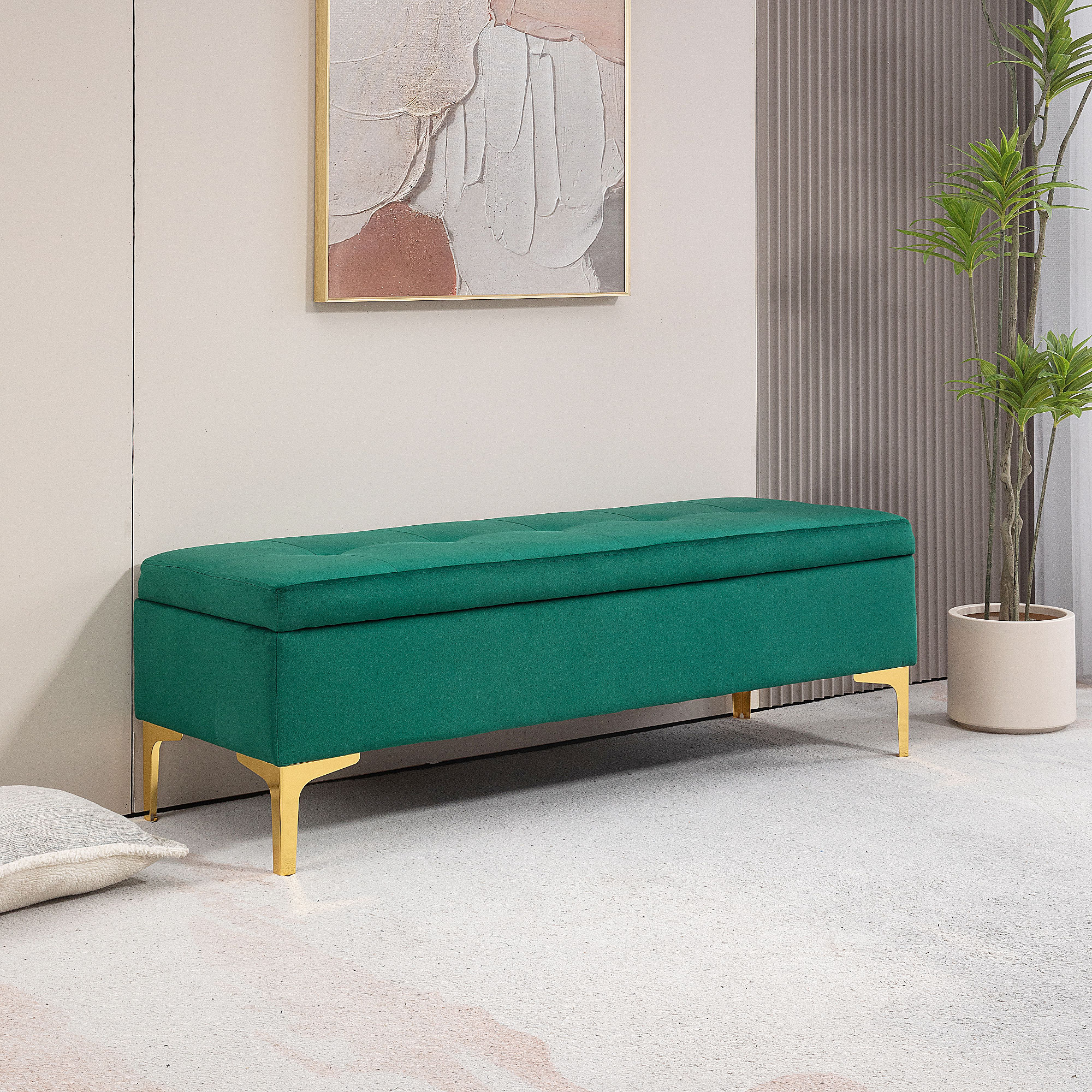 Eine grüne Aufbewahrungsbank mit goldenen Beinen. Ein Gemälde hängt an der Wand dahinter und rechts ist eine Pflanze.
