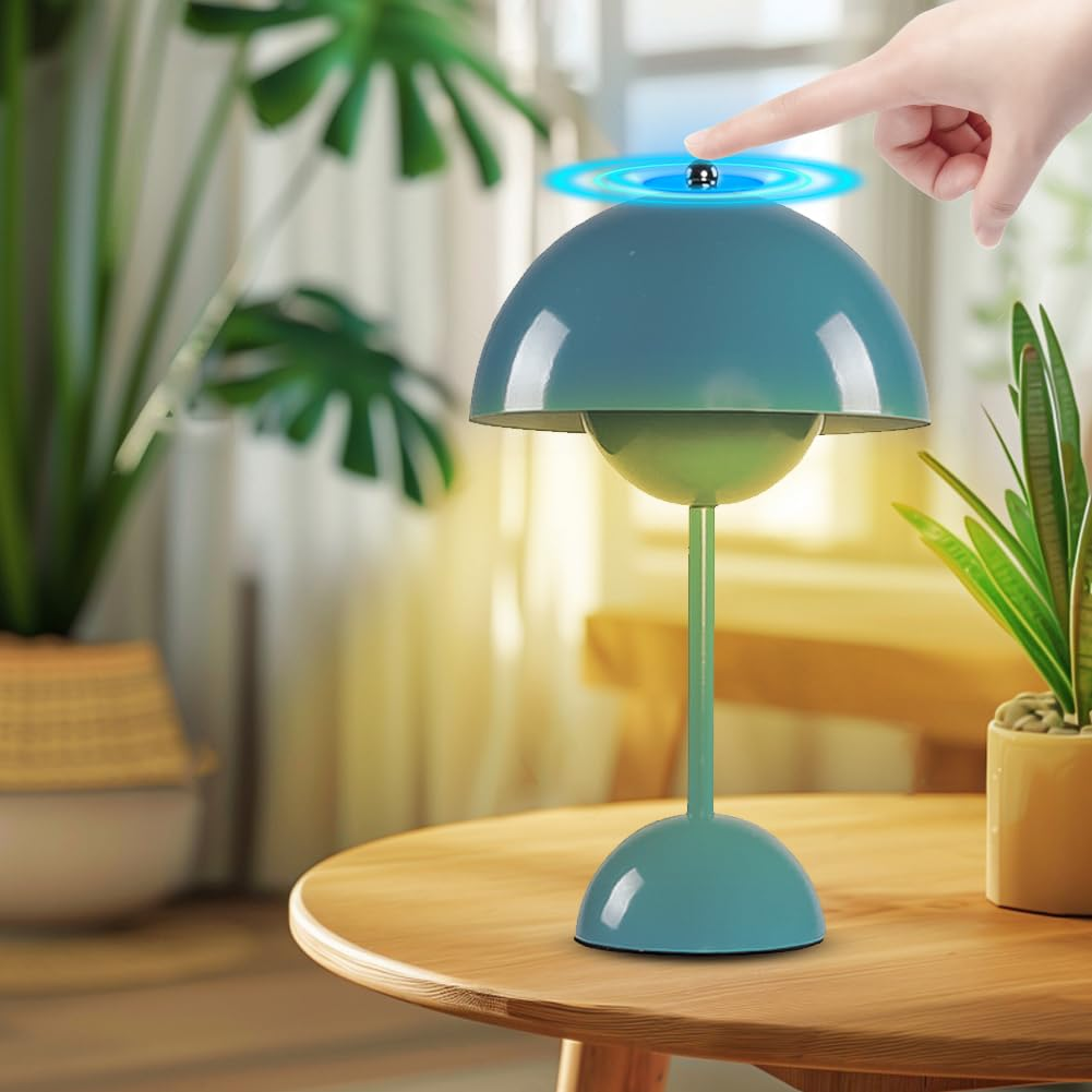 Eine türkisfarbene Lampe, die von einer Hand berührt wird. Die Lampe steht auf einem Holztisch. Grüne Pflanzen im Hintergrund.