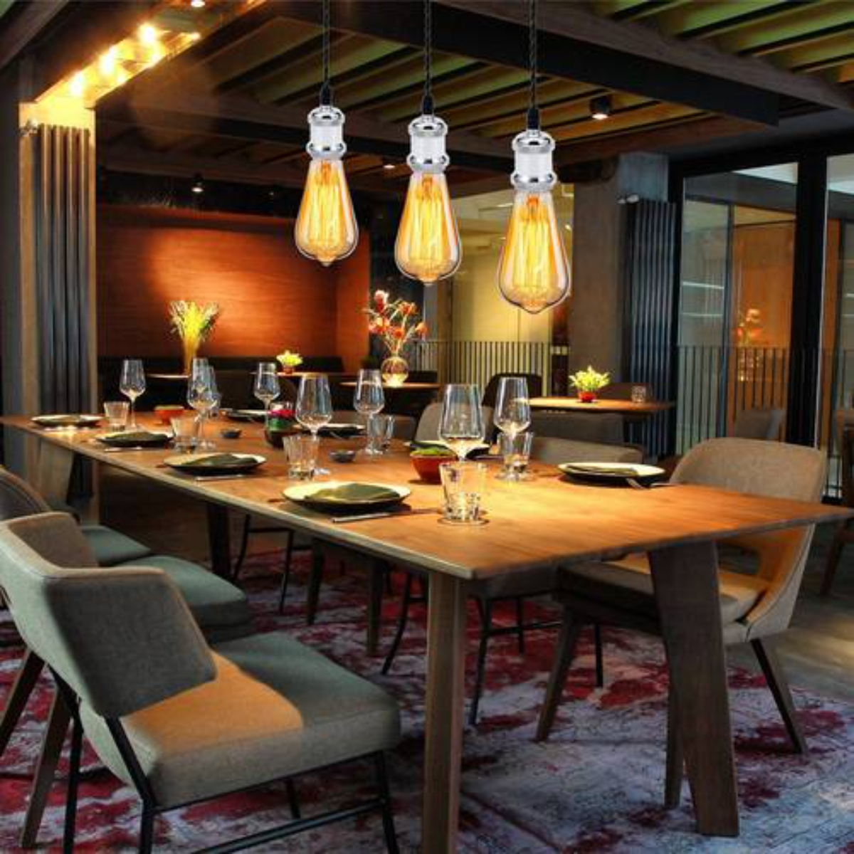 Restaurantinterieur mit langem Holztisch, Hängelampen und Gedecken. Stühle und Barbereich sichtbar.