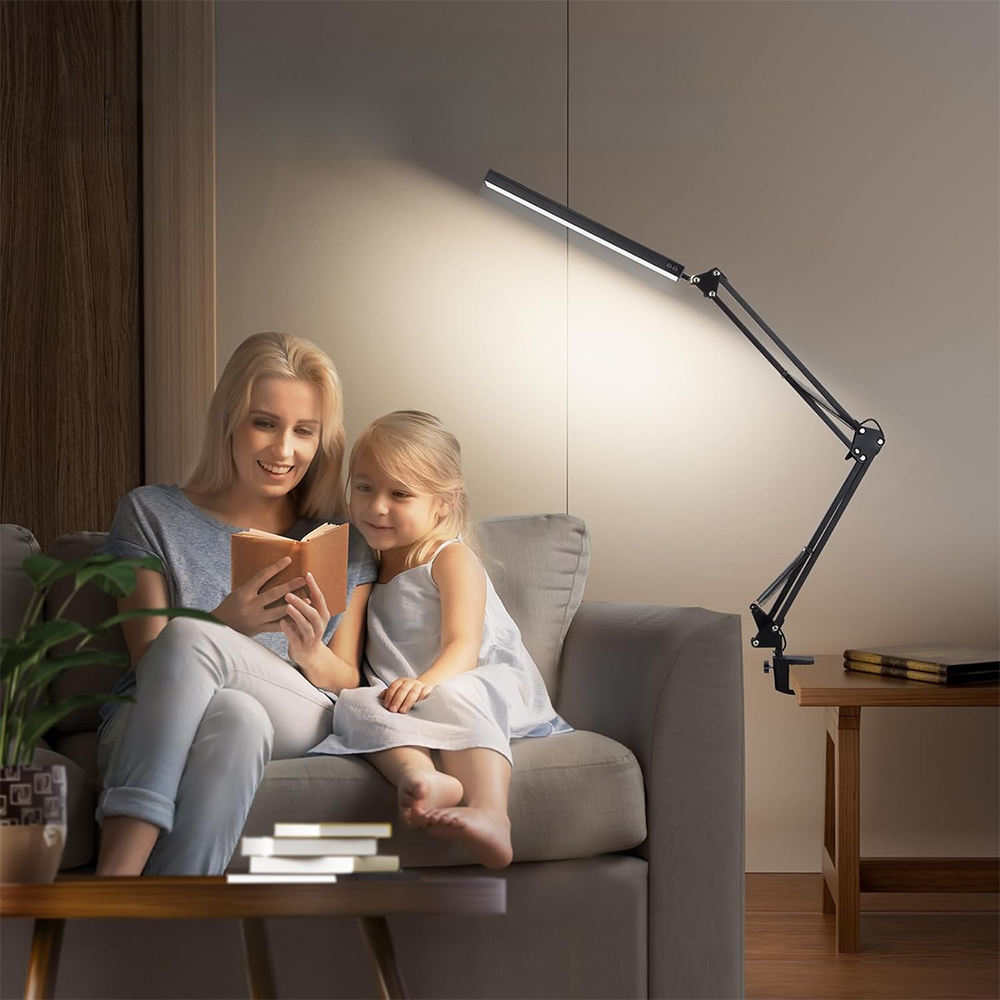 Eine Frau und ein Kind lesen unter einer Schreibtischlampe, neben einem Sofa. Dunkler Hintergrund.