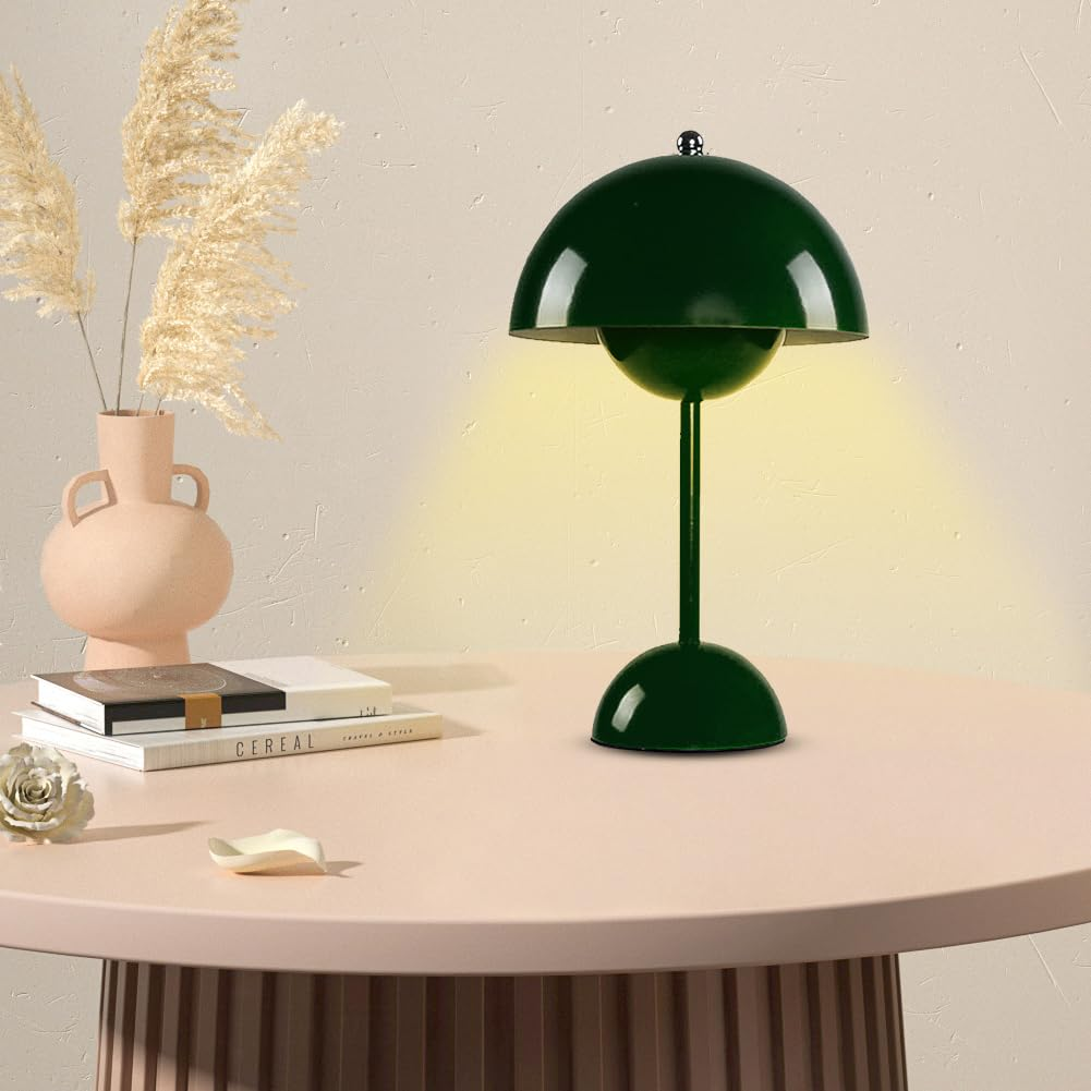 Eine grüne Tischlampe auf einem Tisch. Eine rosa Vase, Bücher und eine weiße Schale stehen neben der Lampe.