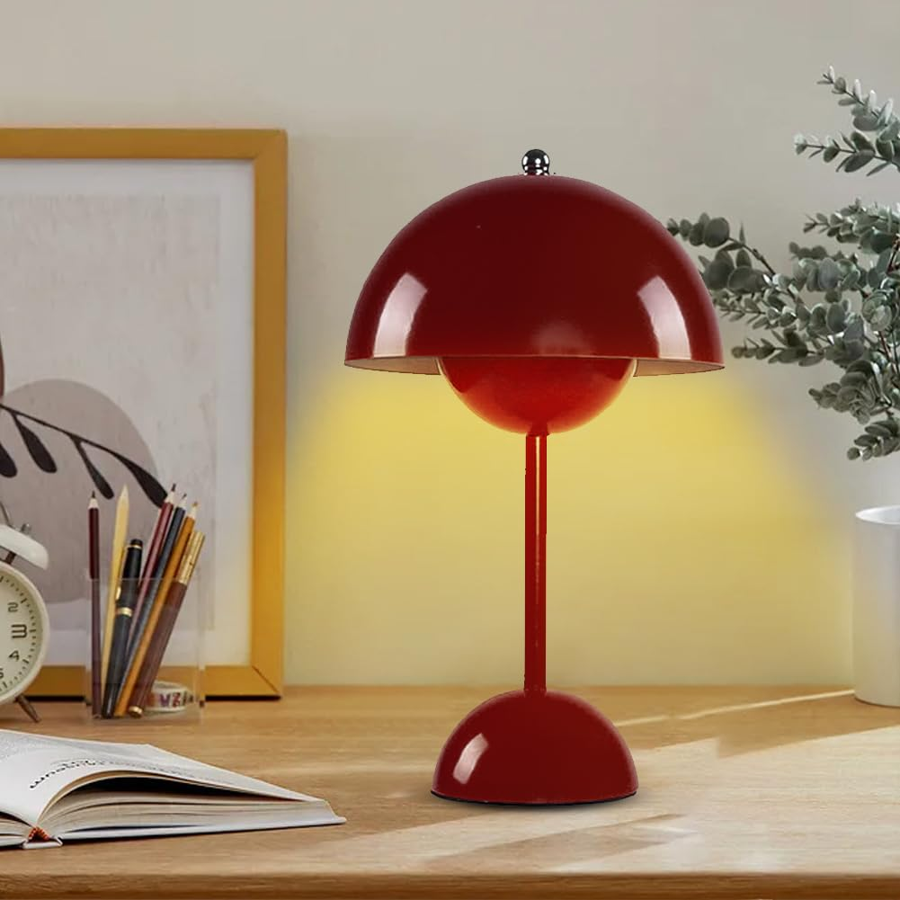 Eine rote Tischlampe auf einem Schreibtisch. Ein Buch, Bleistifte und andere Gegenstände liegen auf dem Schreibtisch.