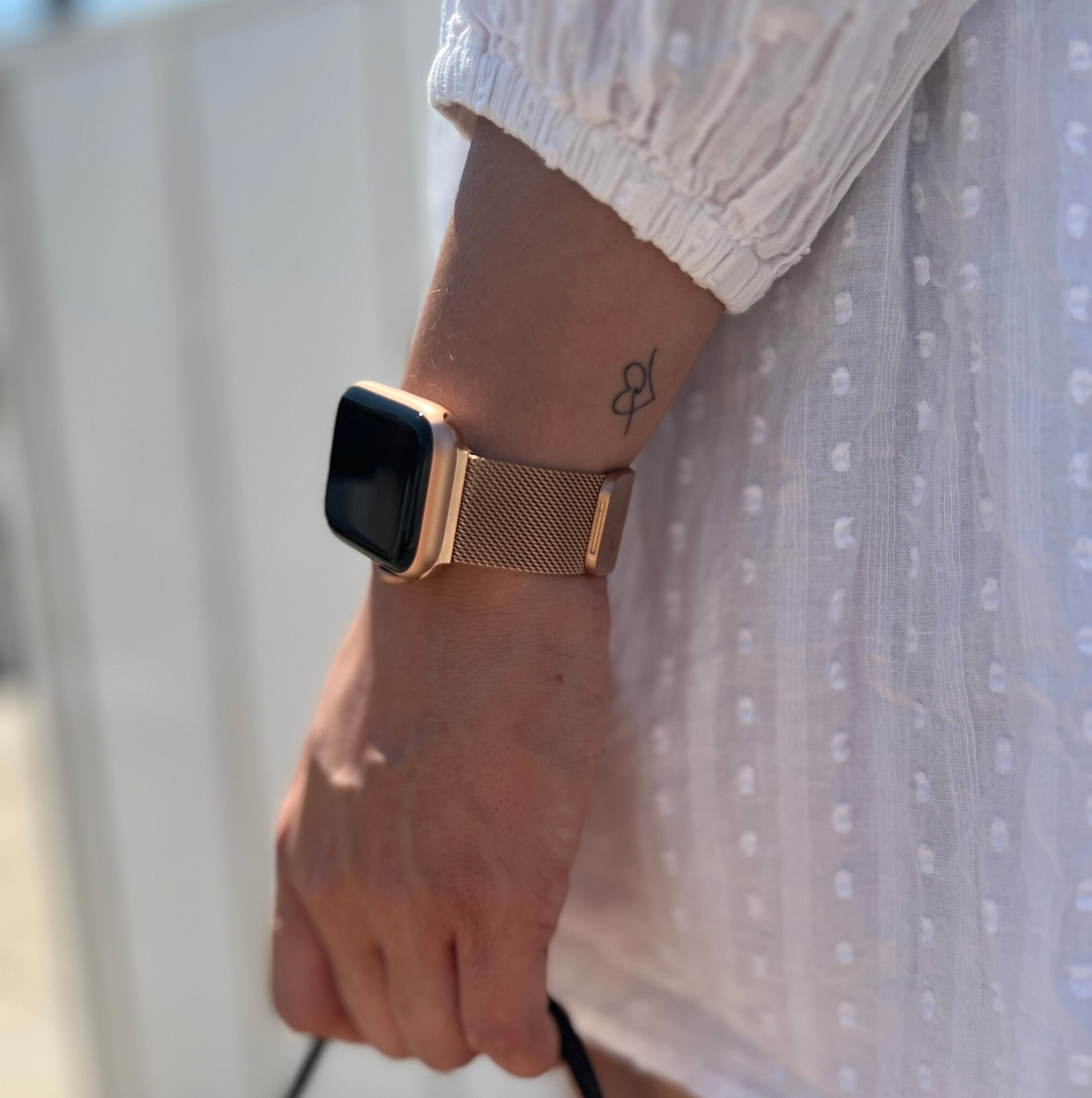 Eine goldene Uhr an einem Handgelenk mit Tattoo, vor einem weißen Kleid.