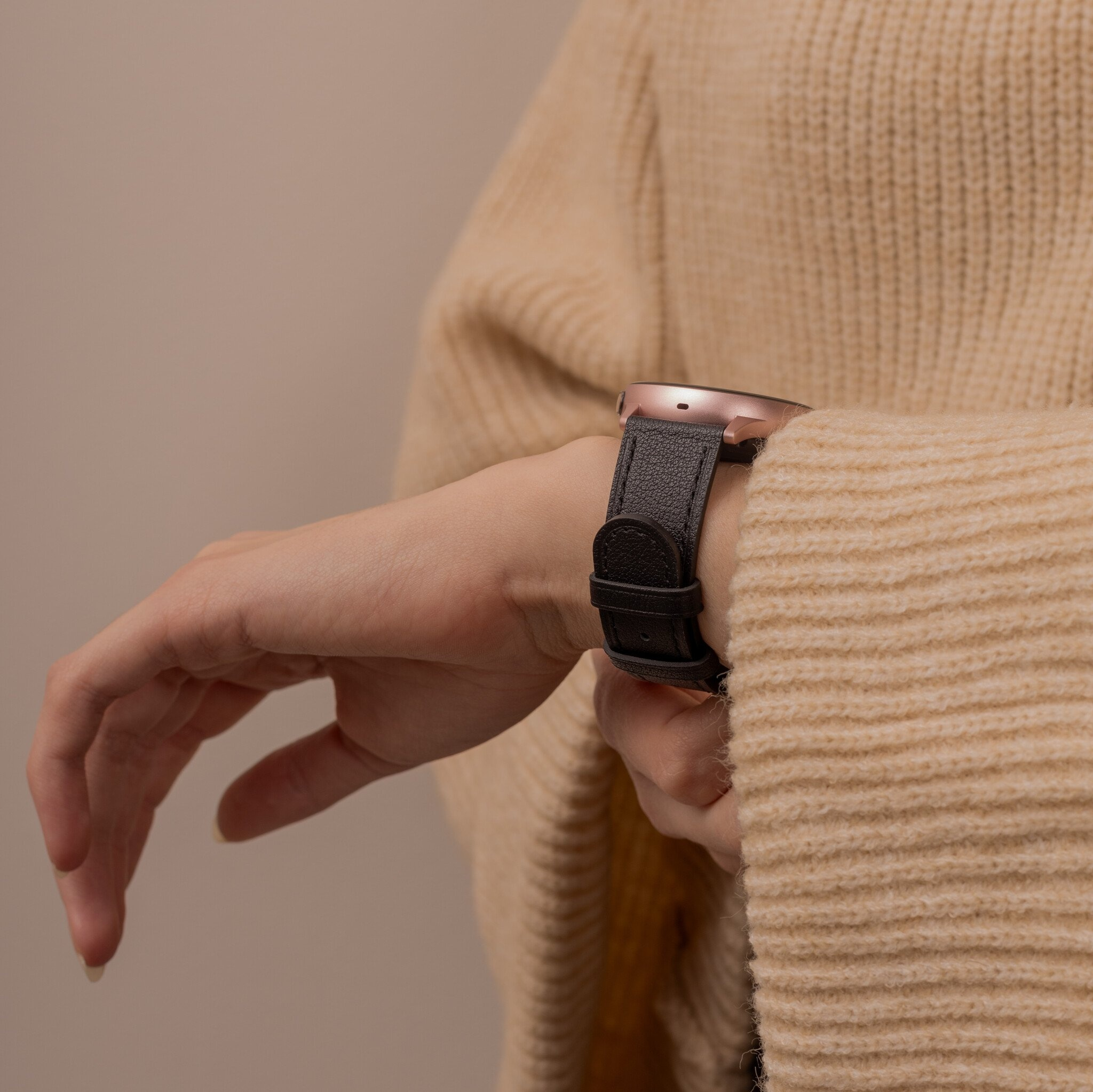 Das Handgelenk einer Person mit roségoldener Uhr und schwarzem Lederarmband.