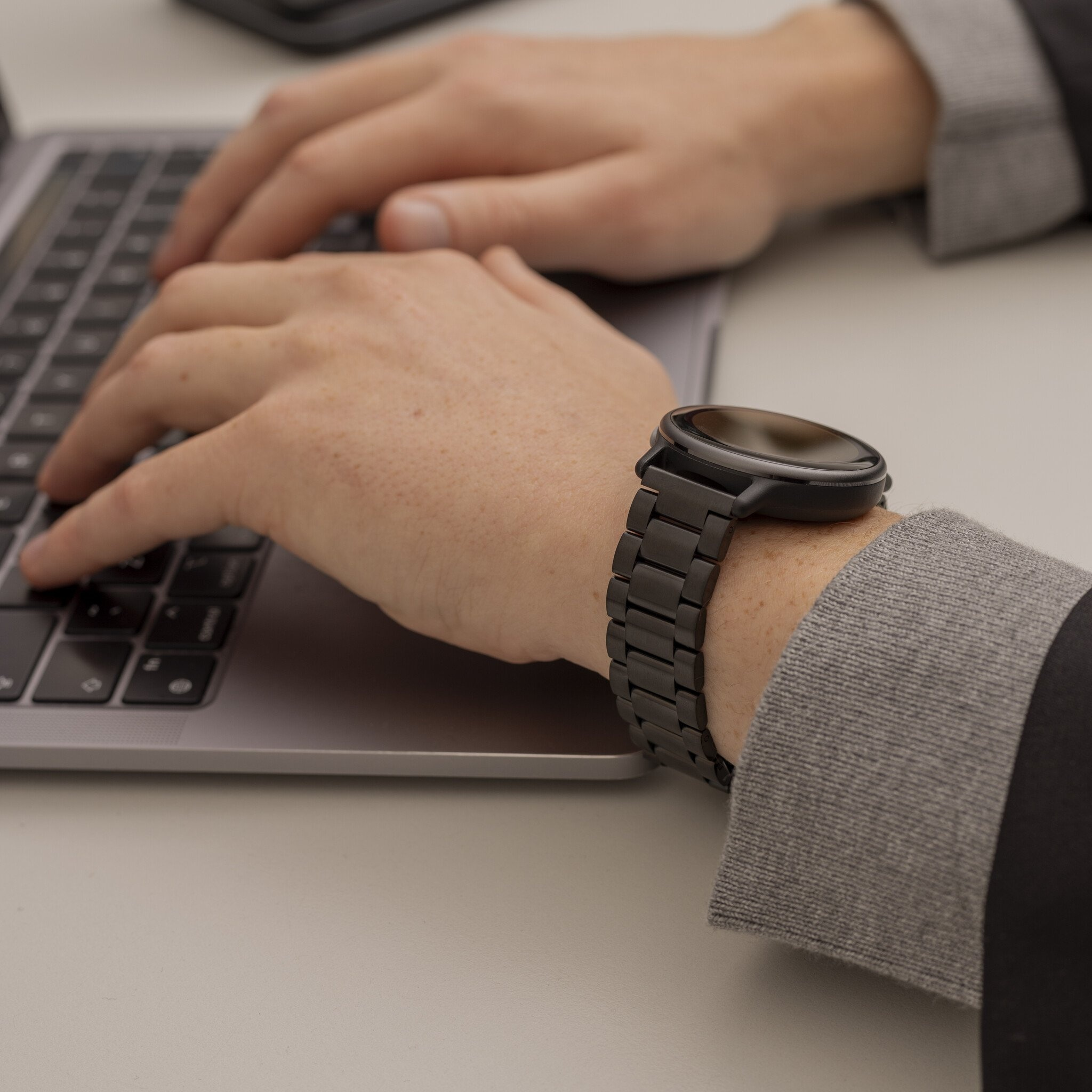 Eine Person, die auf einem Laptop tippt, mit einer schwarzen Uhr am Handgelenk.