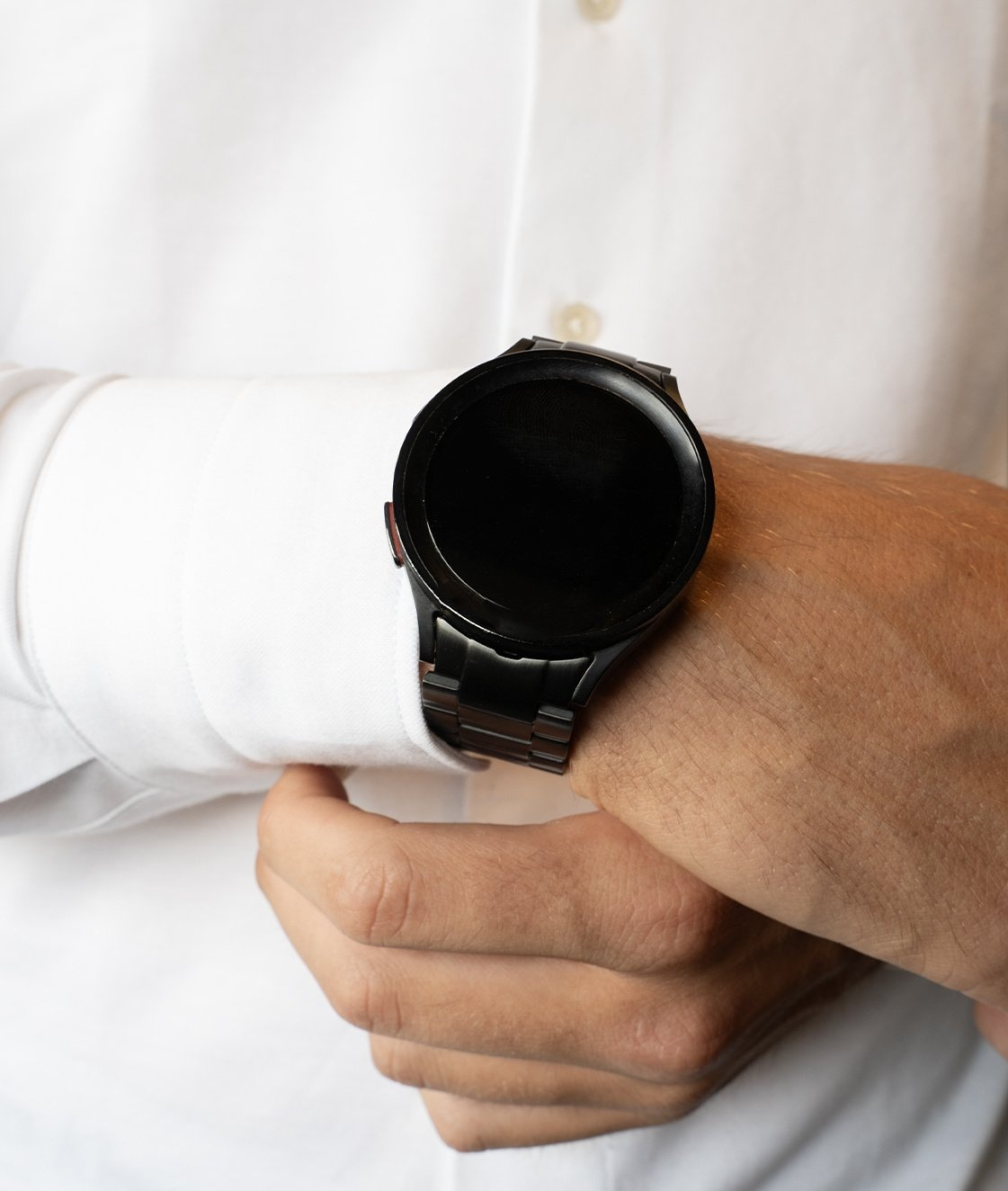 Eine schwarze Uhr an einem Handgelenk, teilweise unter einem grauen Pulloverärmel sichtbar.
