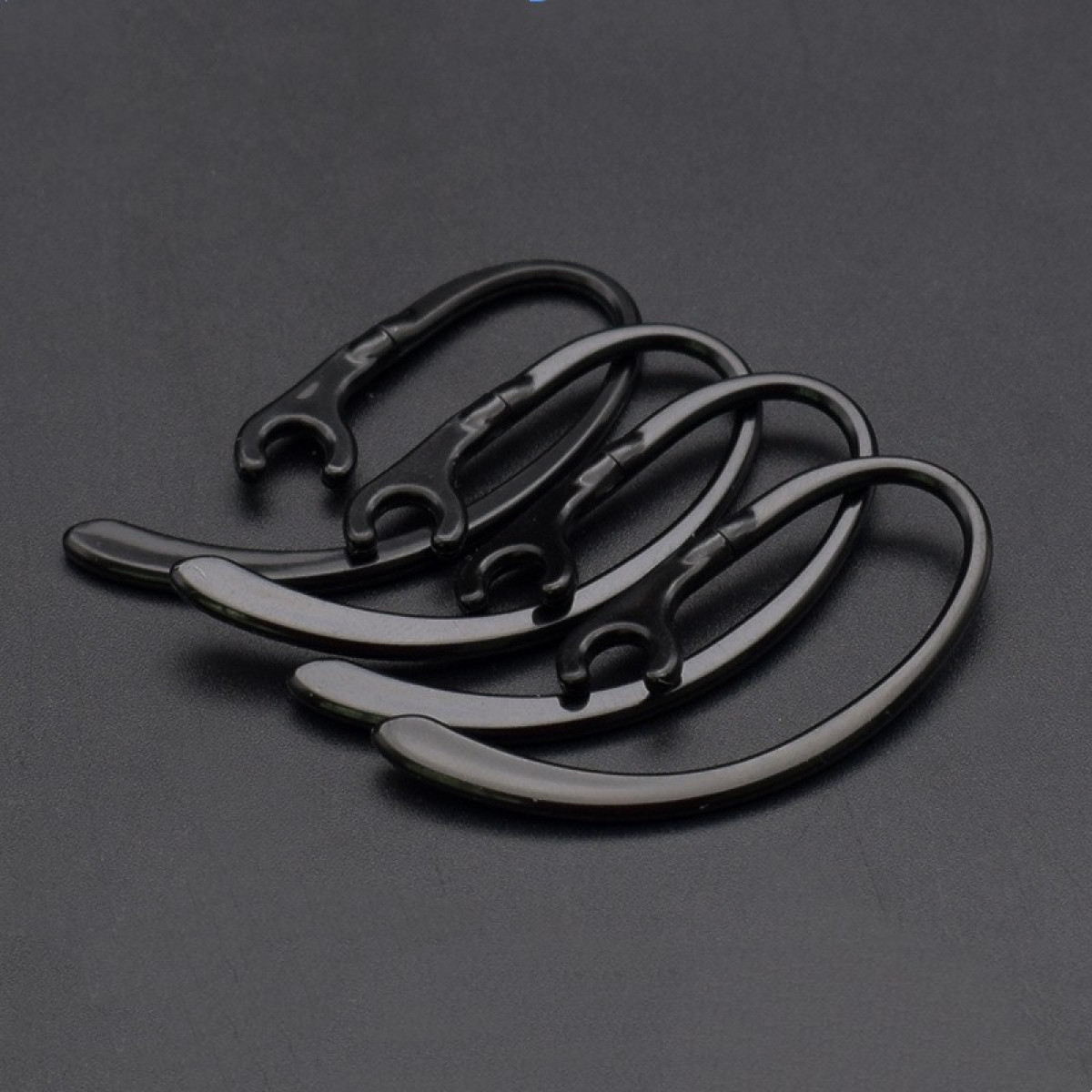 Trzy czarne haczyki na ucho na ciemnej powierzchni. Zakrzywione i z małą pętlą na końcach.