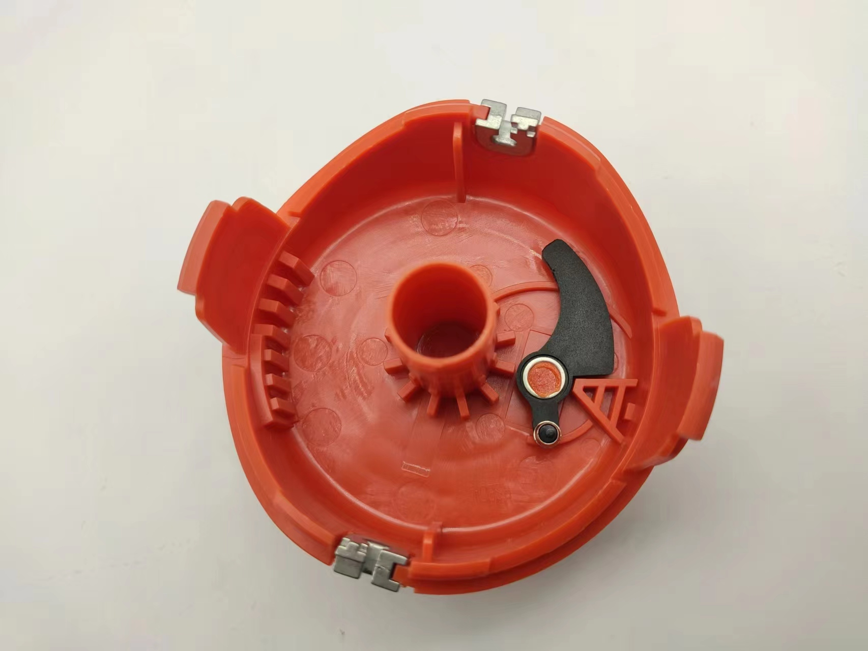 Pomarańczowe, plastikowe wnętrze głowicy trymera z czarnymi elementami mechanicznymi.