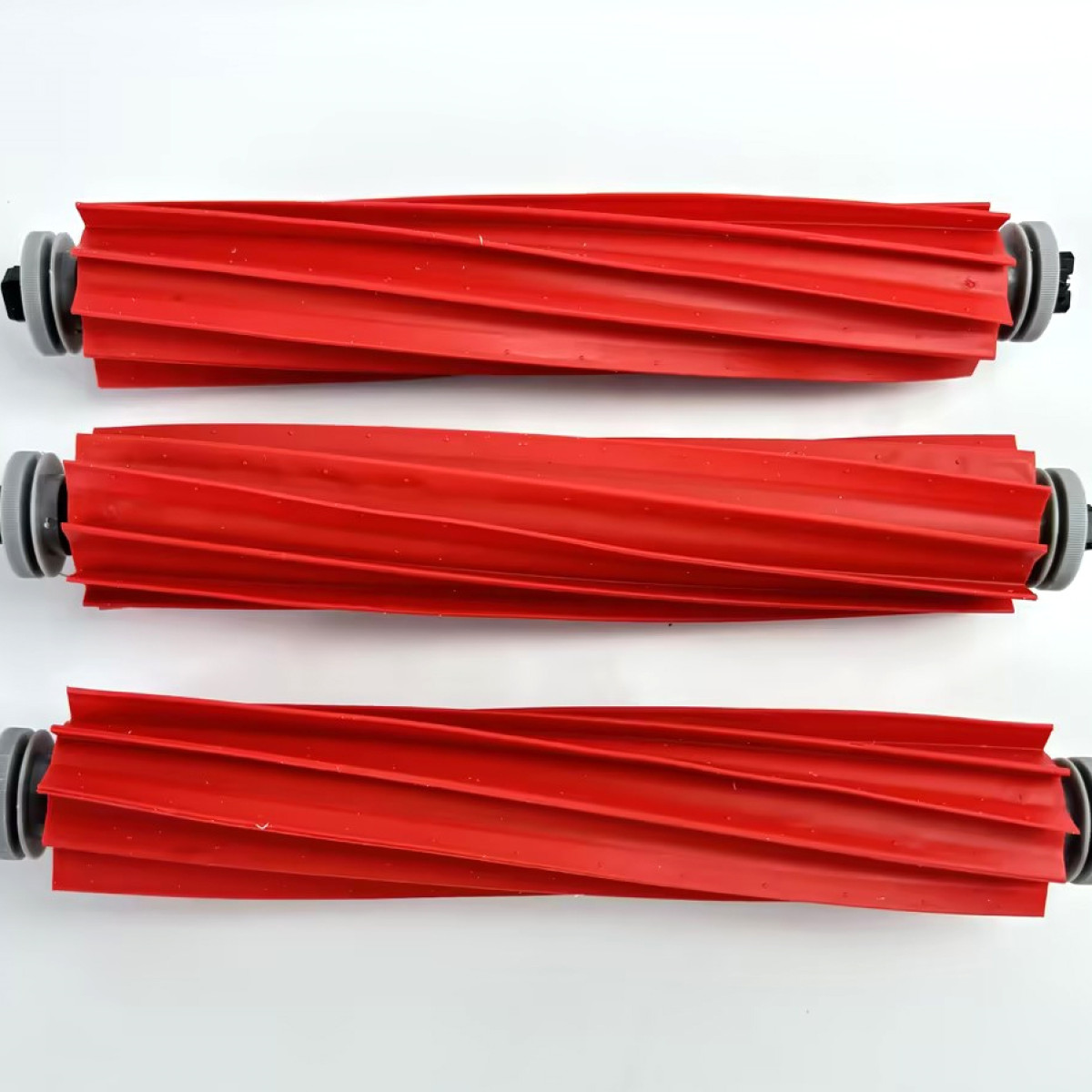 Trzy czerwone szczotki rolkowe do odkurzacza. Są cylindryczne z żebrowanym wzorem.