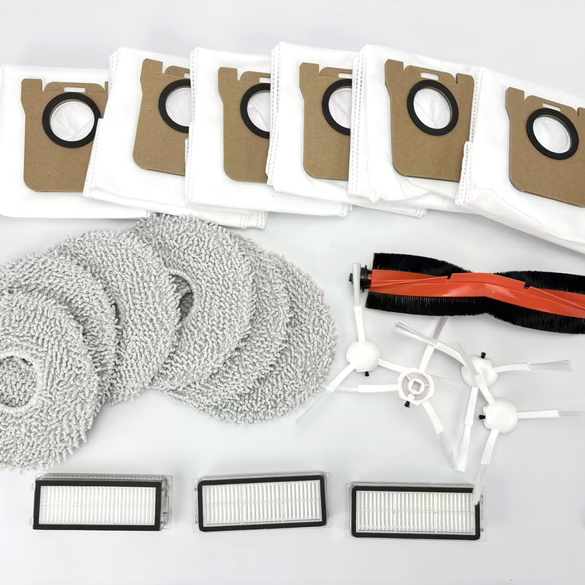 Części do robota odkurzacza, w tym worki, mopy, filtry i szczotki, ułożone na białej powierzchni.