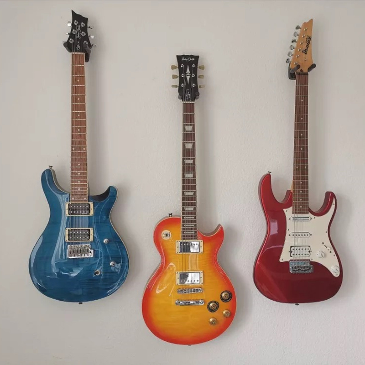 Trois guitares sont accrochées à un mur blanc. Elles ont des couleurs différentes.