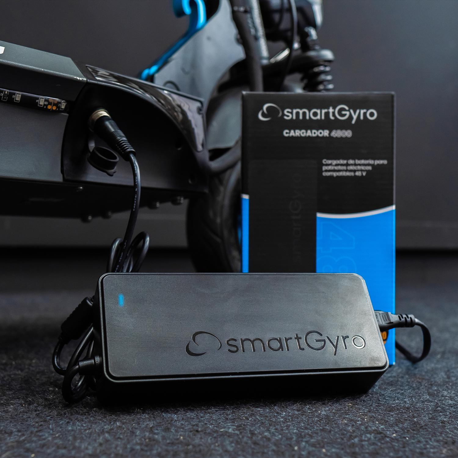Cargador SmartGyro negro con un scooter y una caja de la misma marca, sobre fondo oscuro.