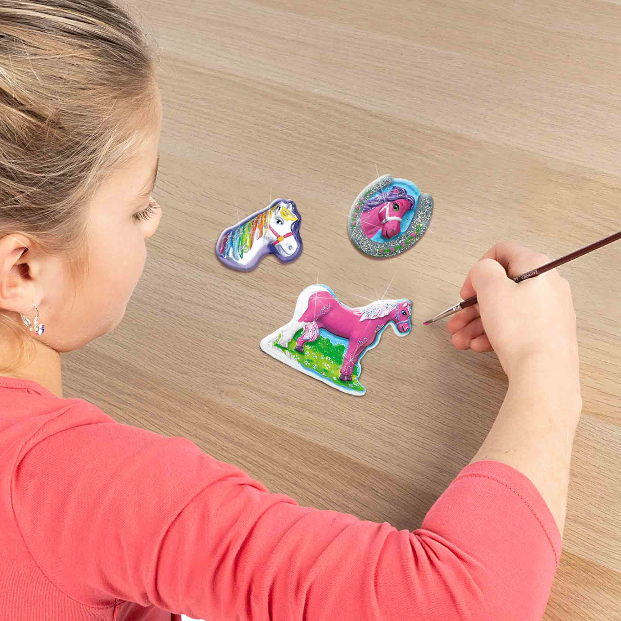 Dziecko malujące figurki koni, z wieloma figurkami na stole.