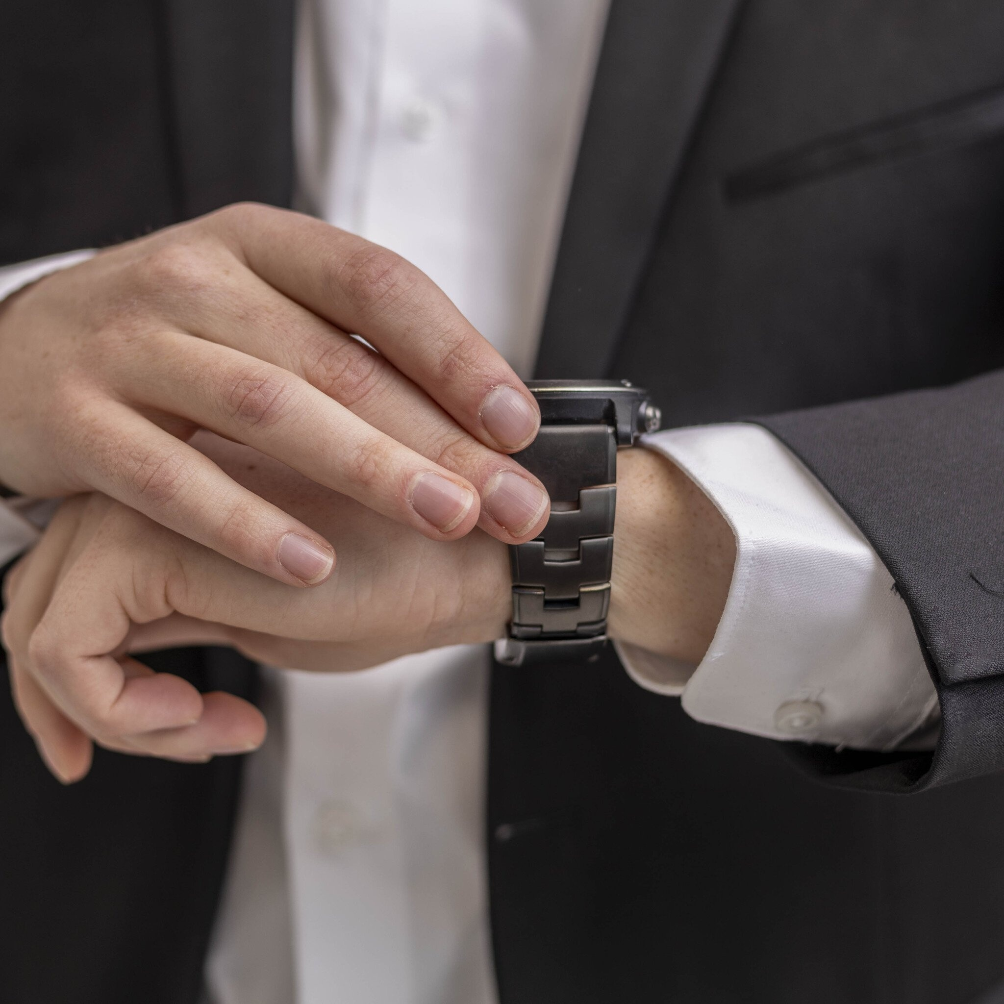 Person passt schwarze Uhr am Handgelenk an. Trägt Anzug, weißes Hemd und Jacke. Nahaufnahme.