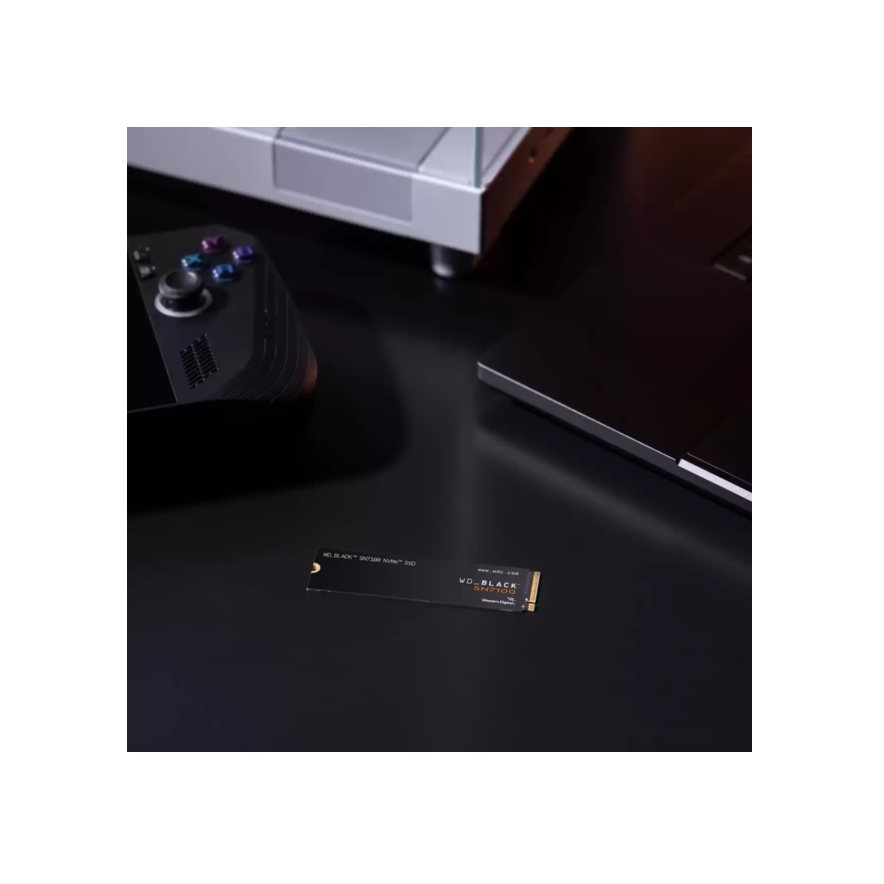 WD_BLACK SN740 SSD na czarnej powierzchni z konsolą do gier i laptopem w tle.