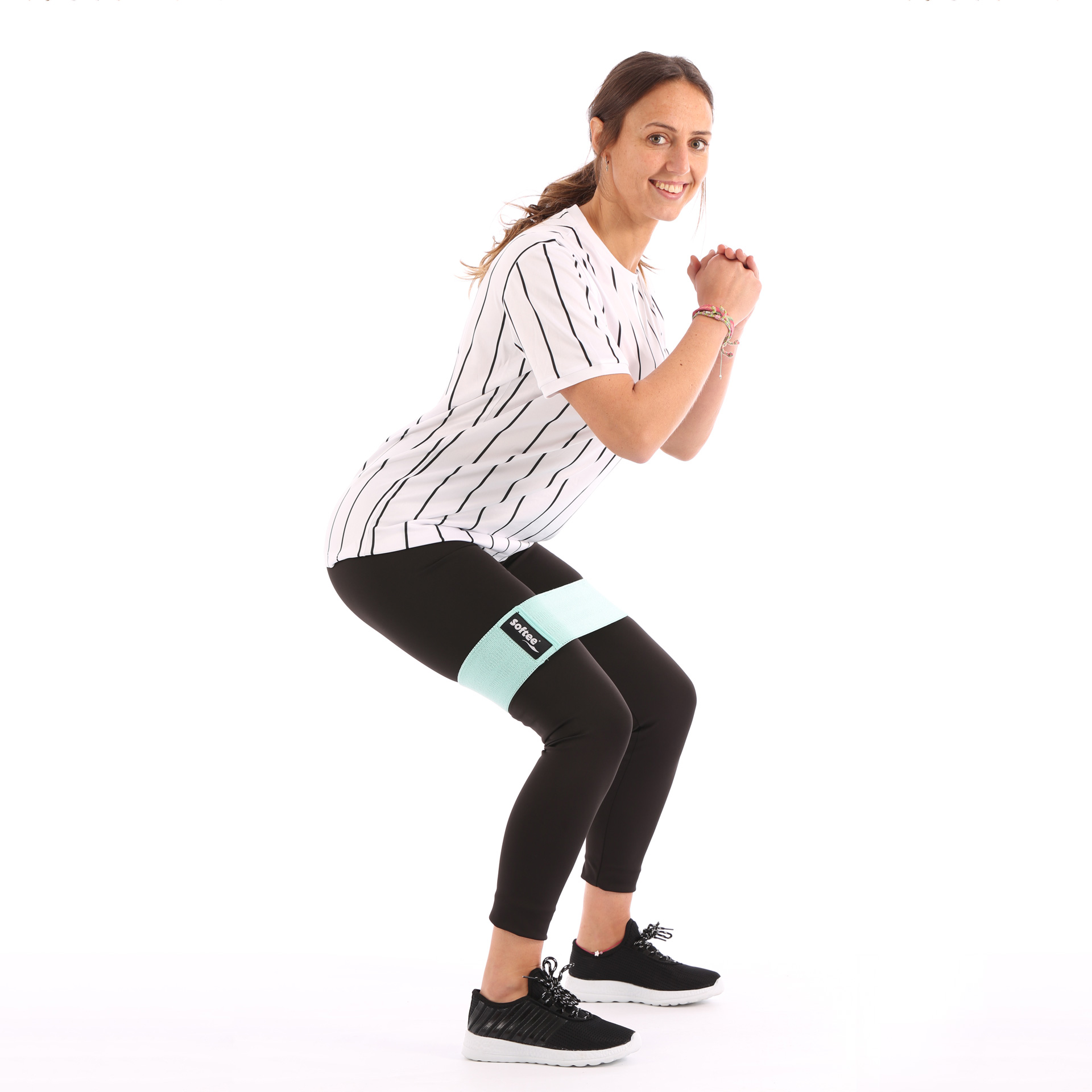 Donna in squat, leggings neri e camicia bianca, usa fascia di resistenza menta. Sfondo bianco.