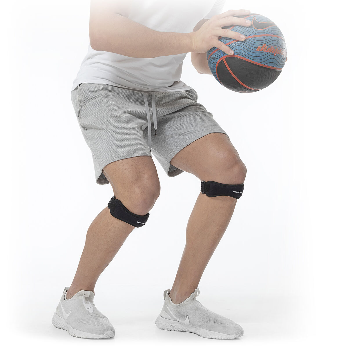 Uomo in pantaloncini e scarpe grigie tiene un pallone da basket e indossa ginocchiere.