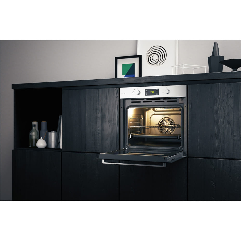Un forno con la porta aperta è integrato in un mobile nero. Sopra ci sono oggetti decorativi.
