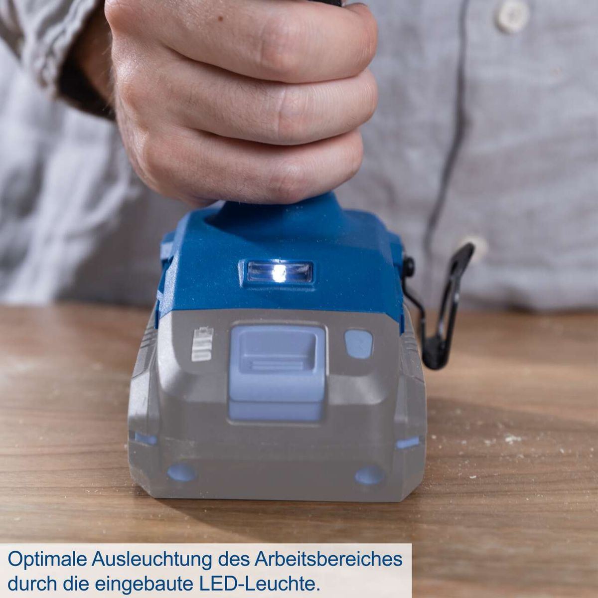 Ręka trzymająca wiertarkę udarową, bateria świeci na drewnianym stole.